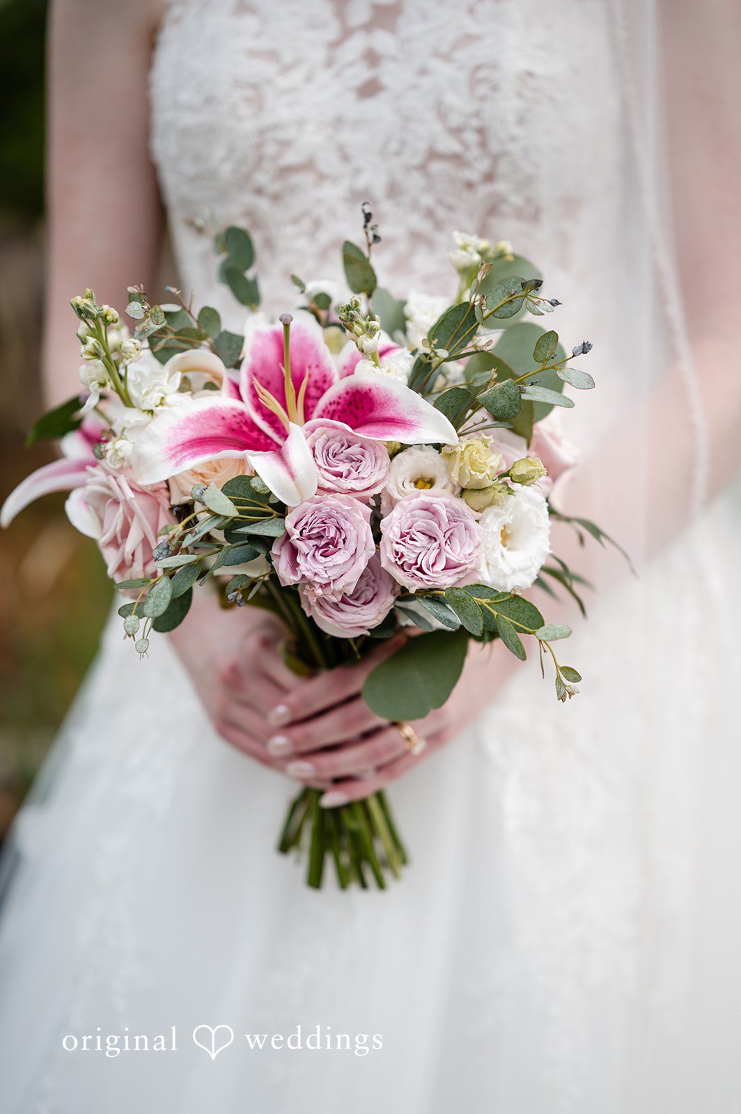 Aislyn + Alex Close-up of a bride holding a bouquet of pink lilies and green leaves.