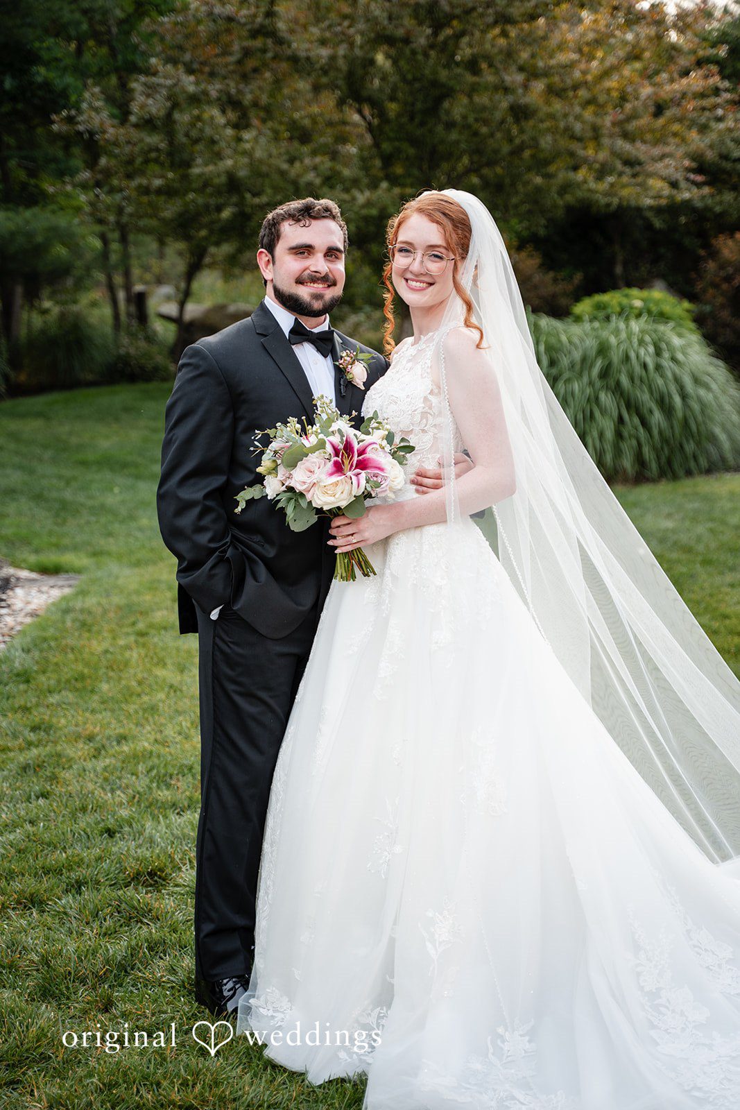 Aislyn + Alex Groom holding the bride from behind as they pose together in a garden.
