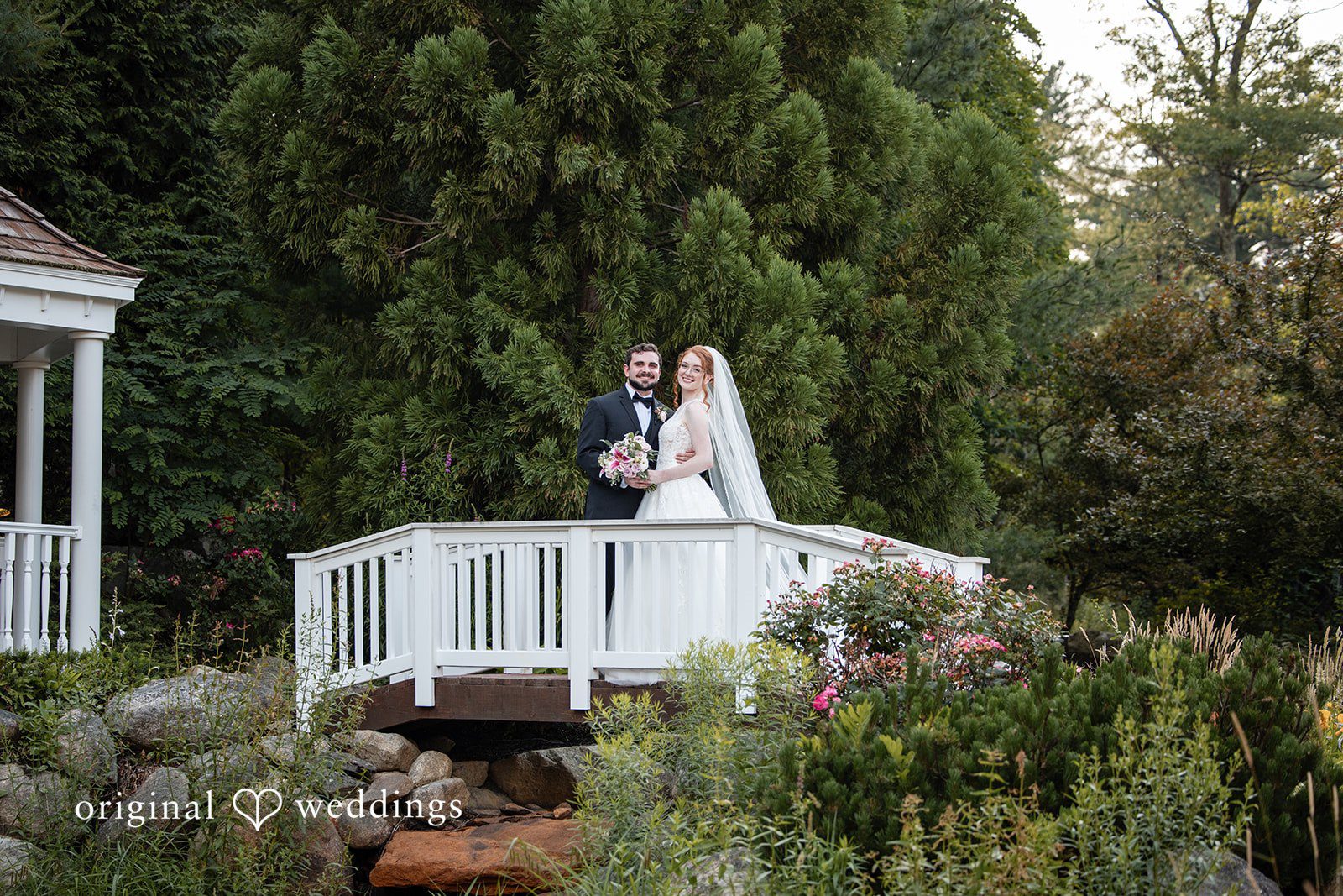 Aislyn + Alex Bride and groom posing together on an elevated white gazebo structure.