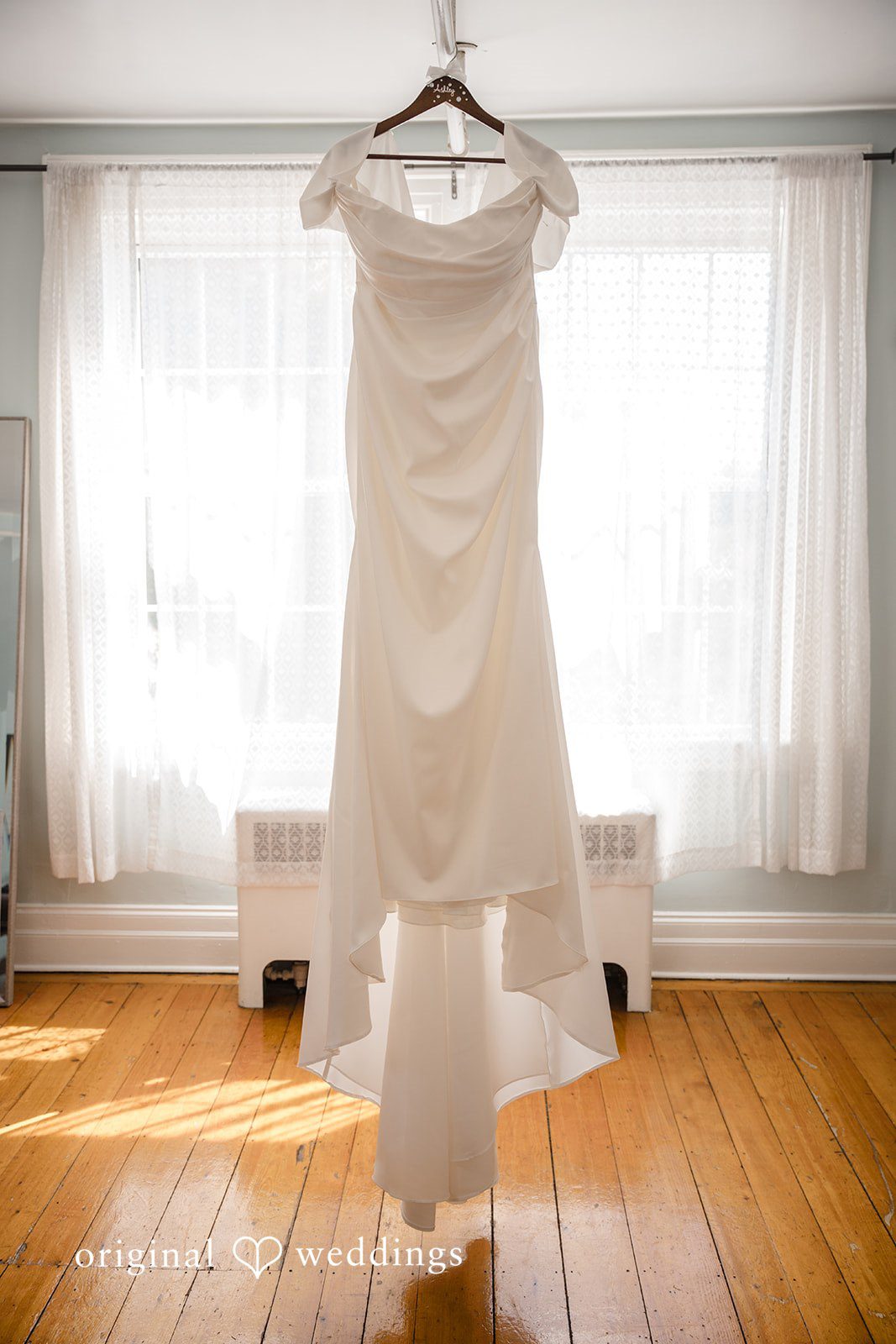 Ashley + Jonathan White wedding dress hanging vertically in front of a bright window.