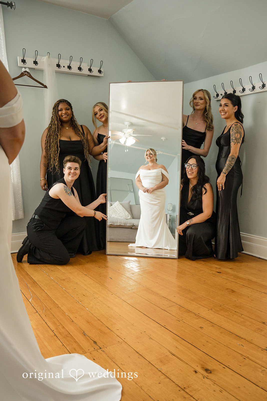 Ashley + Jonathan Group of bridesmaids in black dresses watching the bride put on her dress.