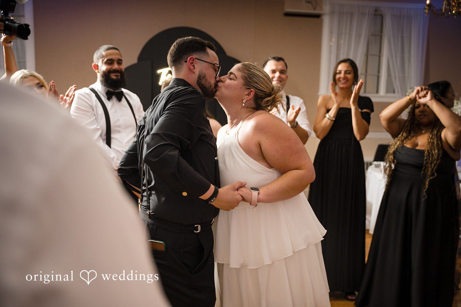 Ashley + Jonathan A bride and groom kissing on the dance floor surrounded by their wedding guests.