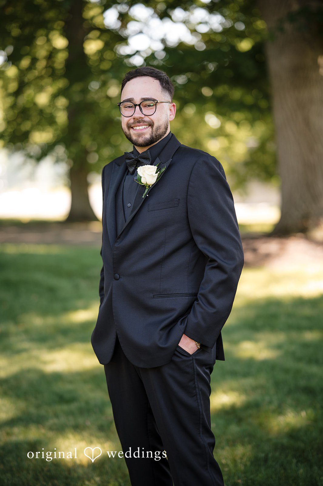 Ashley + Jonathan Smiling groom standing on a lawn wearing a black wedding suit.