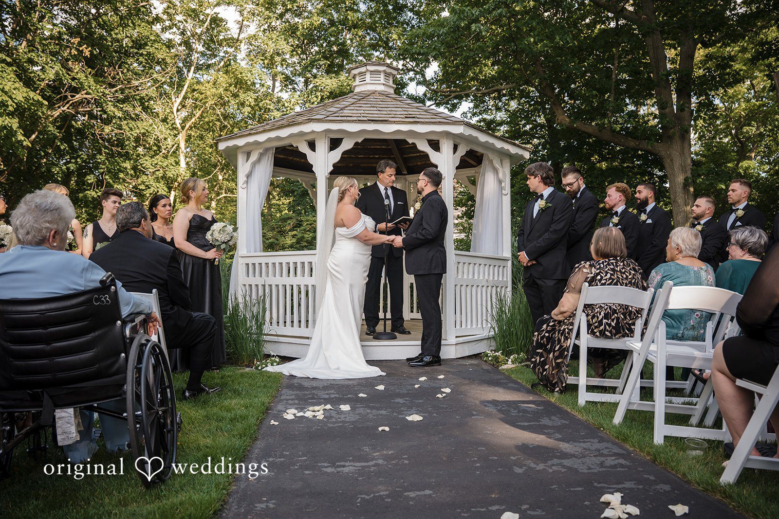 Ashley + Jonathan A bride and groom exchanging vows under a white garden gazebo surrounded by seated guests.