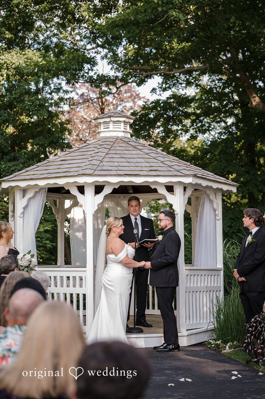 Ashley + Jonathan A bride and groom holding hands under a white gazebo during a wedding ceremony.
