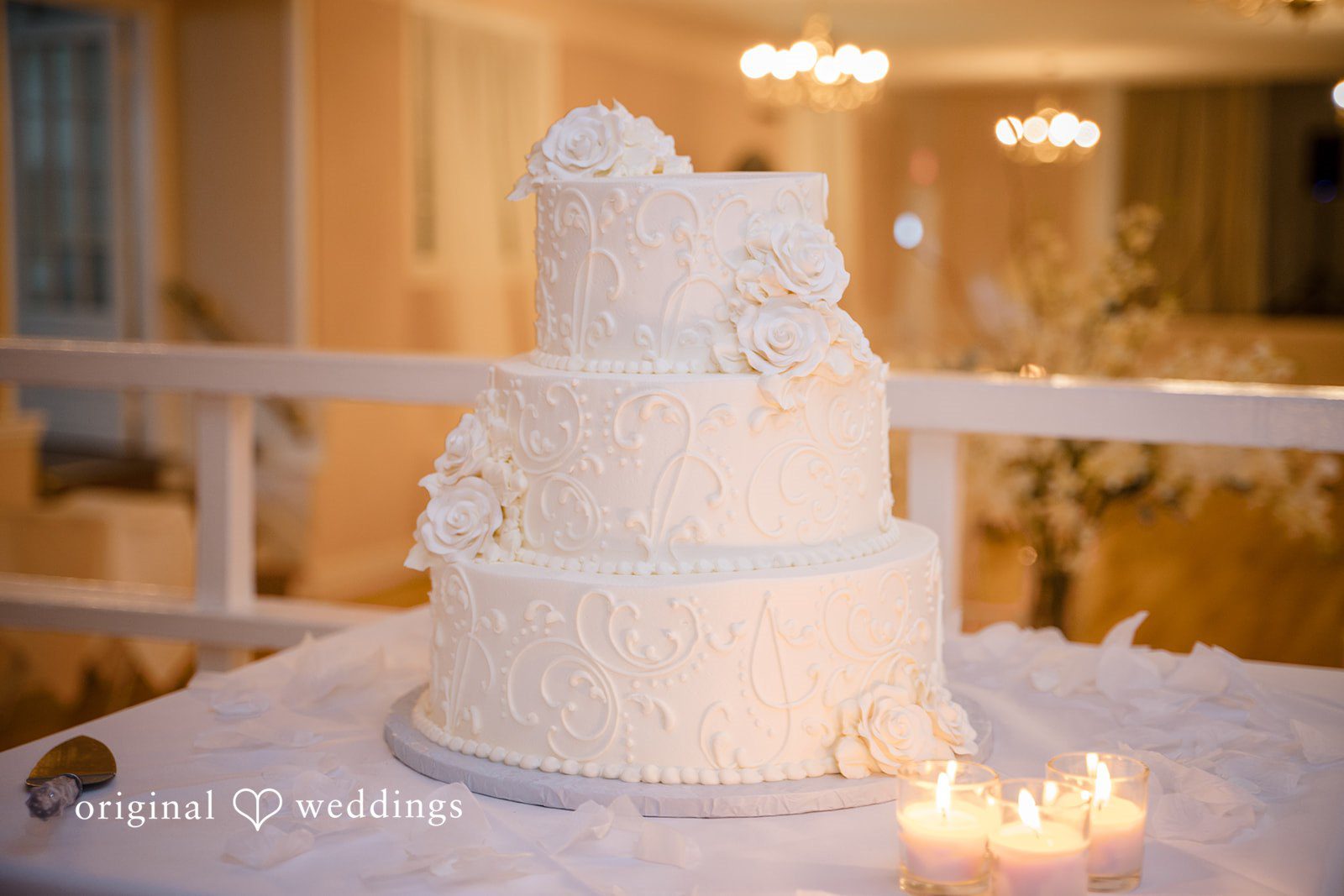Ashley + Jonathan Three-tiered white wedding cake decorated with delicate floral patterns.