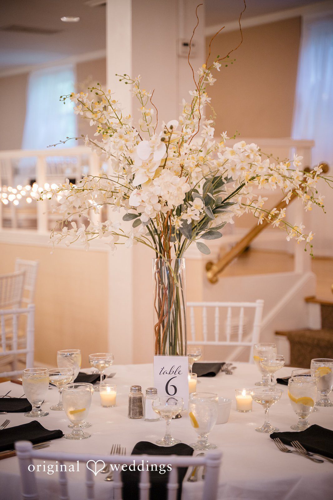 Ashley + Jonathan Reception table featuring a tall floral centerpiece with white blossoms.