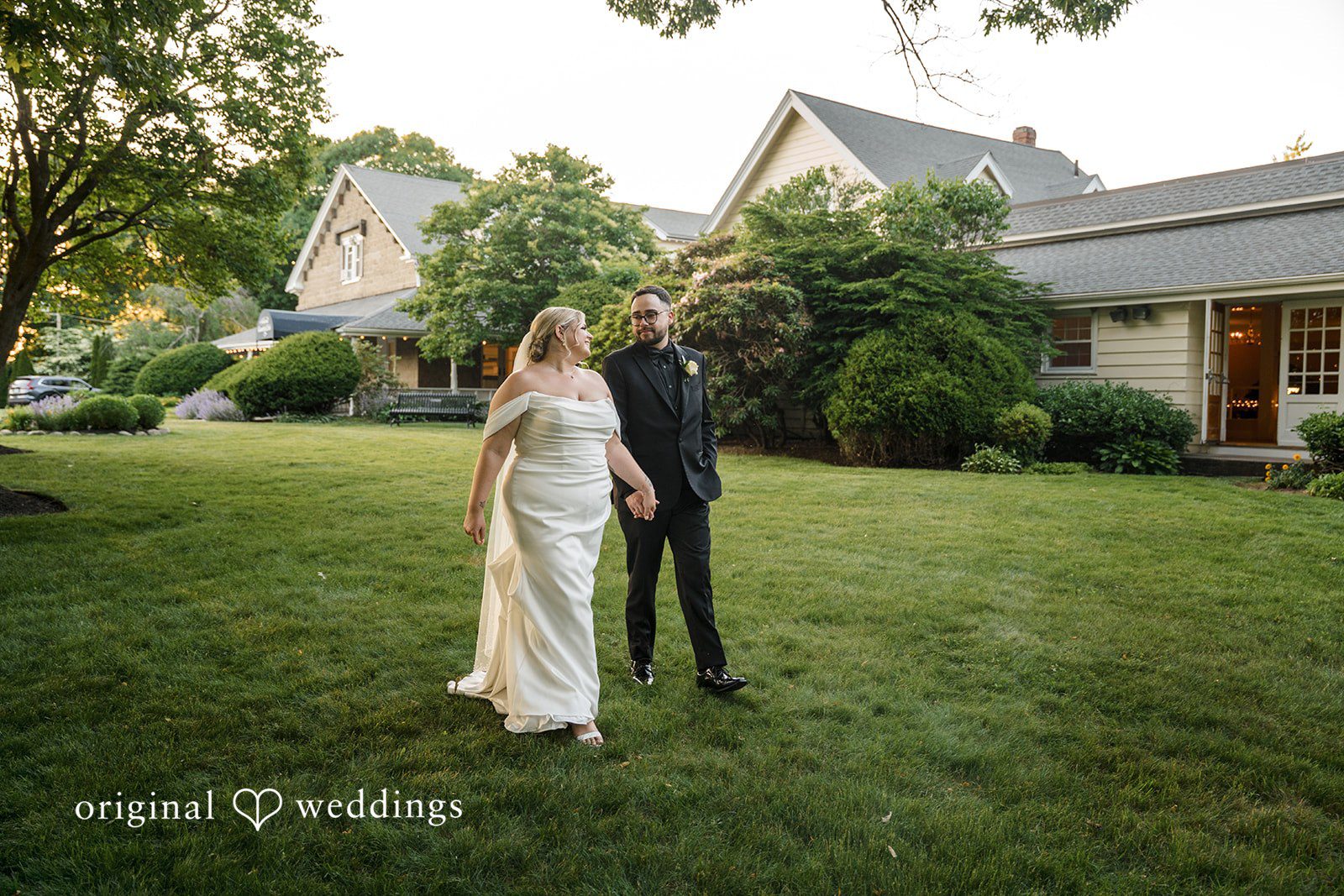 Ashley + Jonathan A bride and groom holding hands while standing together on a lush green lawn.