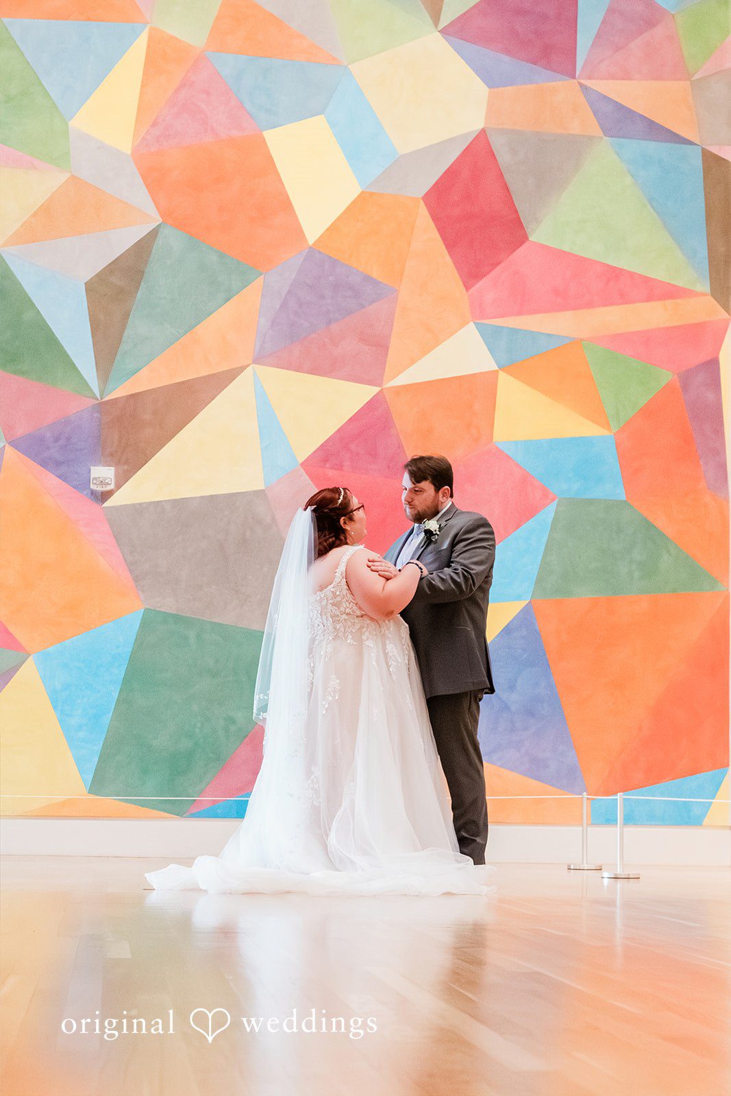 Grace + Nicholas A bride and groom posing in front of a large, colorful geometric mural.