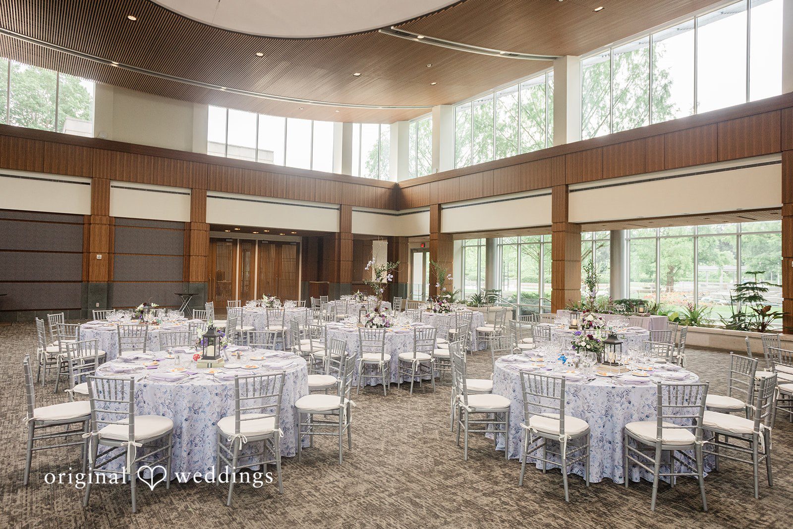 Grace + Nicholas A spacious wedding reception hall filled with multiple round tables draped in silver linens.
