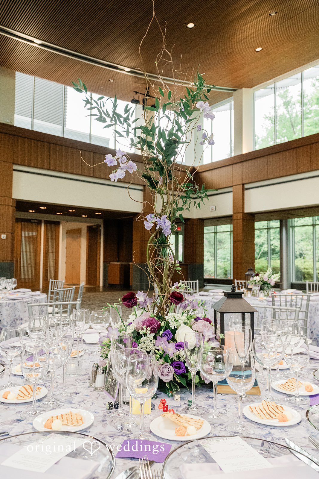 Grace + Nicholas A beautifully set wedding reception table featuring a tall floral centerpiece and elegant place settings.