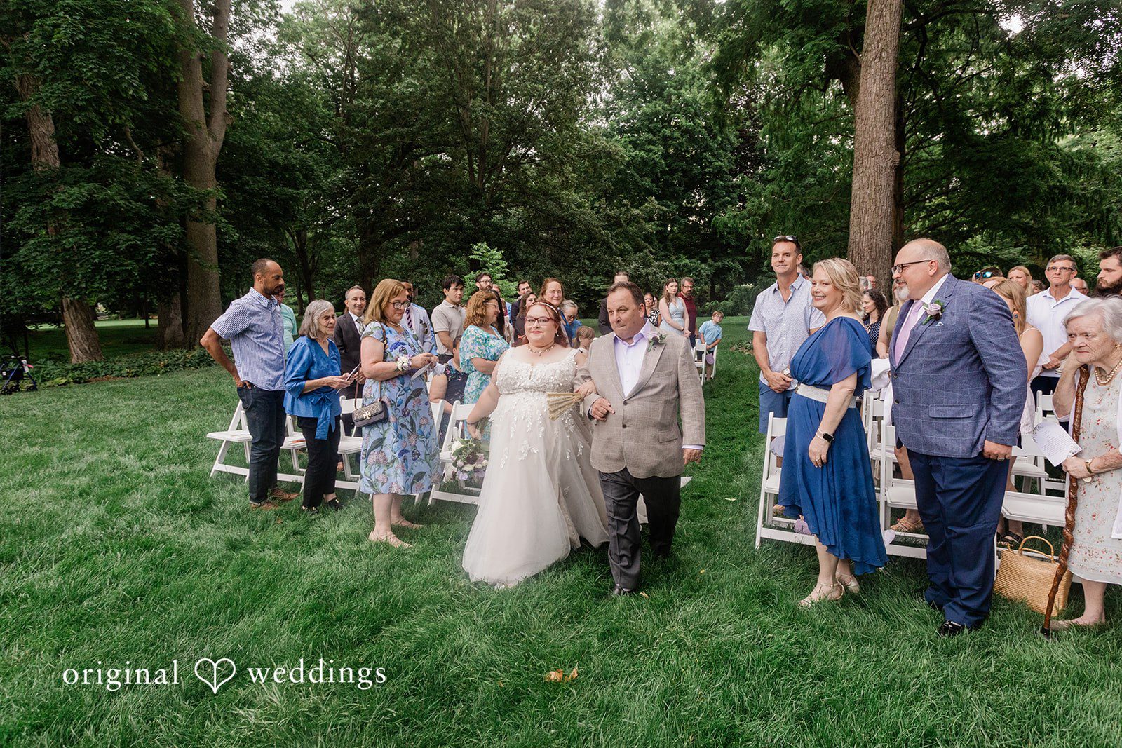 Grace + Nicholas A wide shot of wedding guests gathered on a grassy lawn for a ceremony.