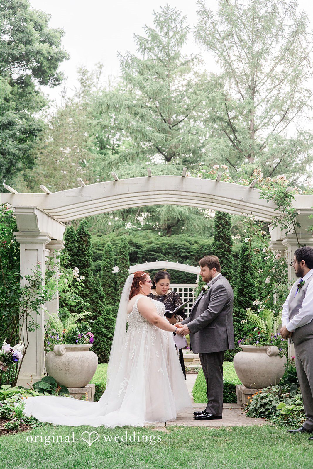 Grace + Nicholas A bride and groom holding hands during their ceremony under a stone archway.