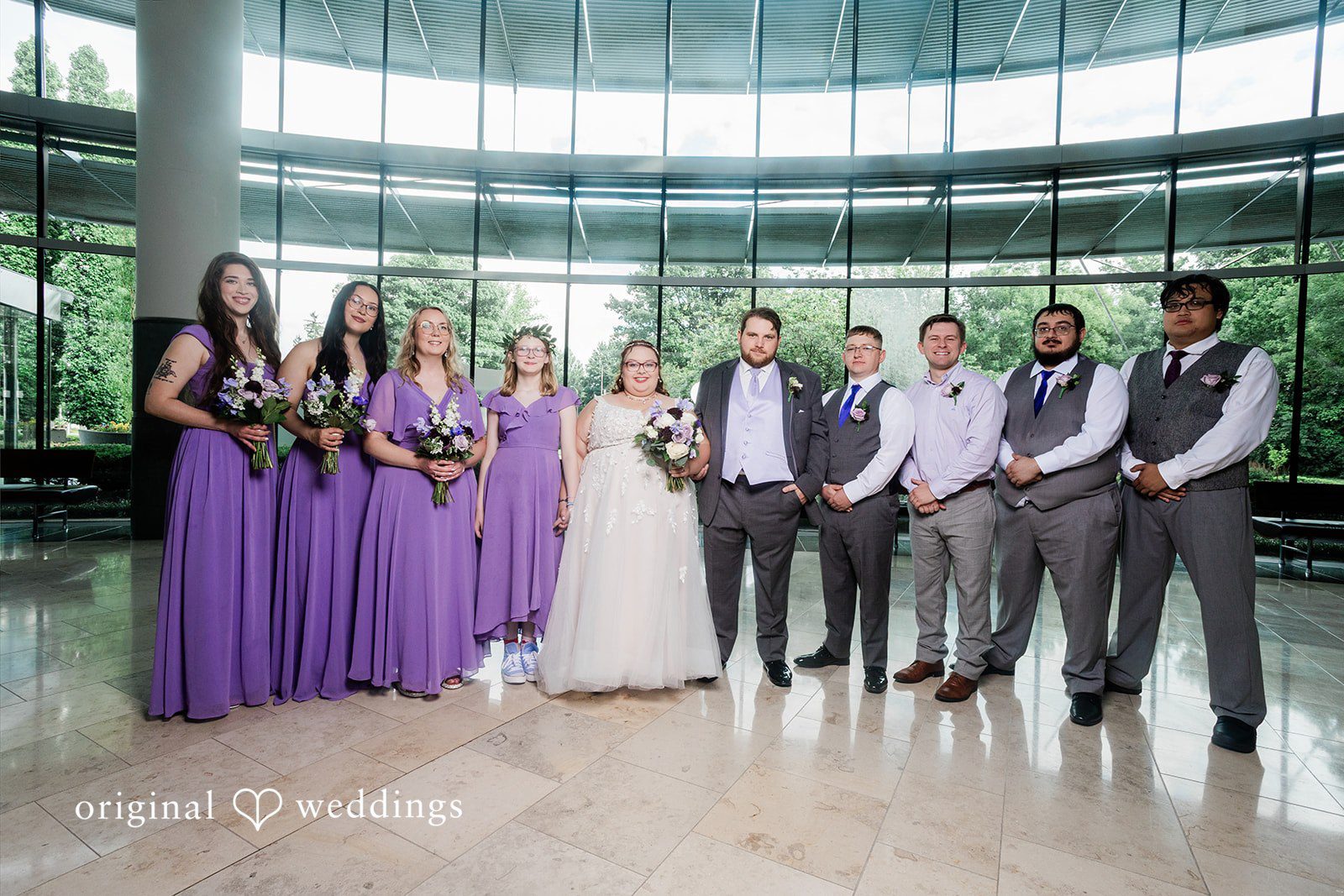 Grace + Nicholas A full wedding party with bridesmaids in purple gowns and groomsmen in gray suits posing together.
