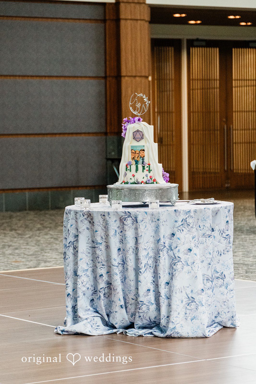 Grace + Nicholas A tiered wedding cake displayed on a table covered in a textured silver tablecloth.