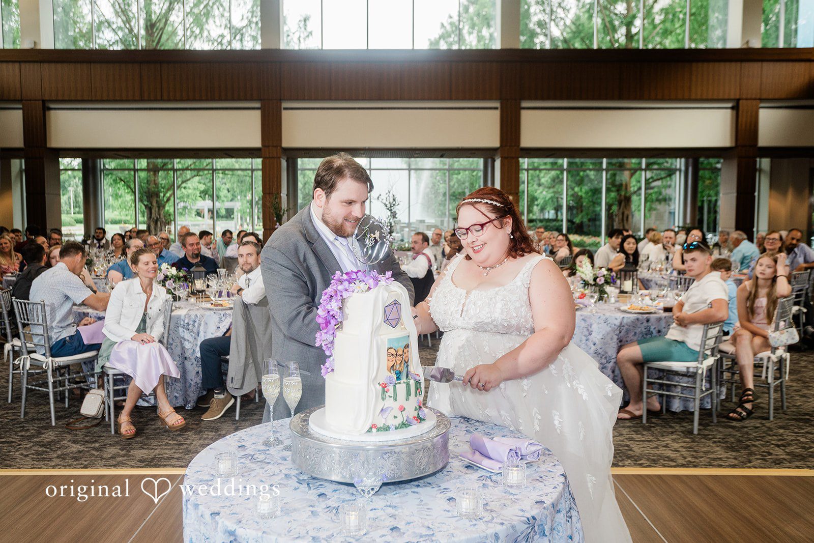 Grace + Nicholas A bride and groom preparing to cut their tiered wedding cake in front of seated guests.