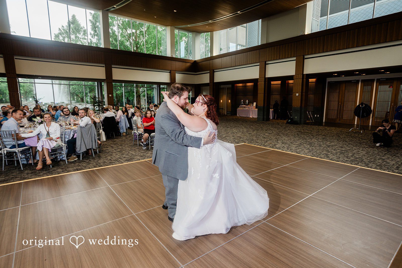 Grace + Nicholas A bride and groom sharing a slow dance on a wooden dance floor surrounded by watching guests.