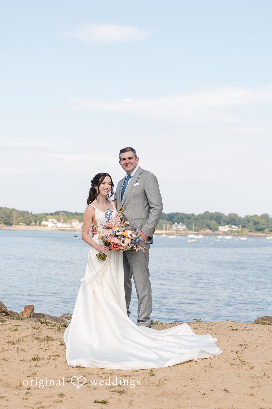 Kerri + David Bride holding a colorful bouquet while standing with the groom beside the ocean at Oceanview of Nahant.