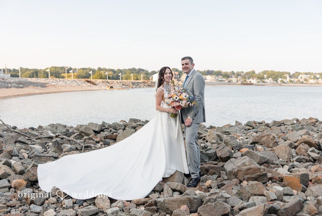 Kerri + David Bride and groom smiling together beside the rocky shoreline at Oceanview of Nahant captured by Boston Wedding Photographers from Original Weddings