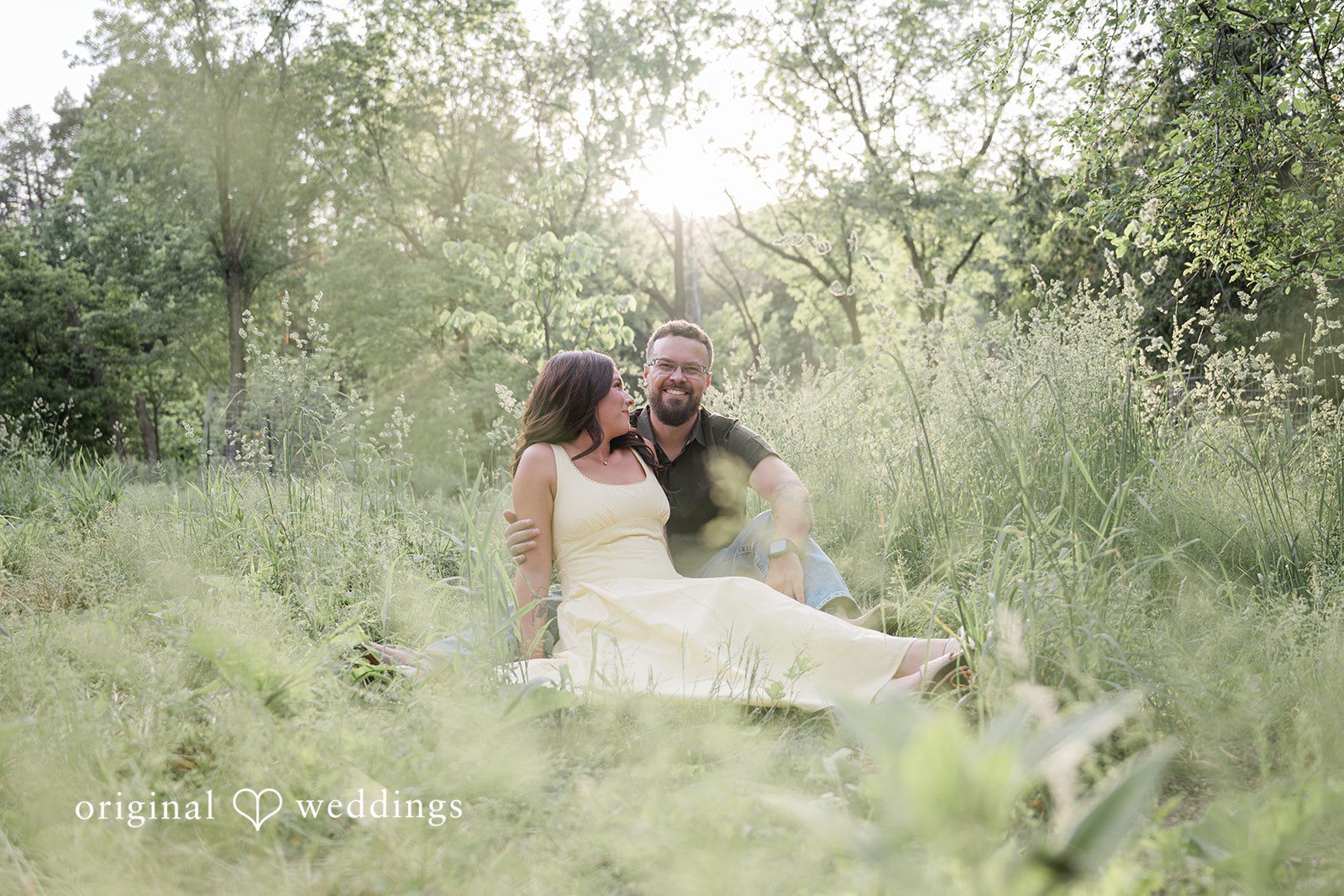 Andrea + Jordan A couple relaxing together in a wide, sunlit field surrounded by tall grass.