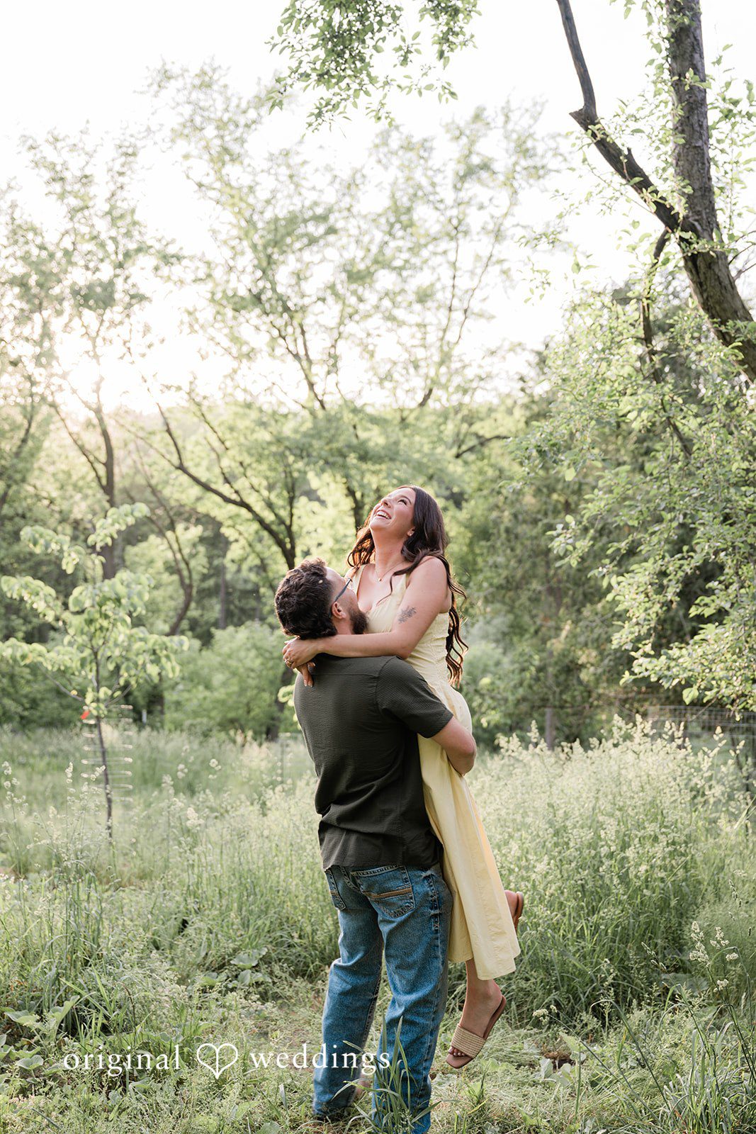 Andrea + Jordan A man lifting a woman in his arms during a joyful embrace in a forest clearing.
