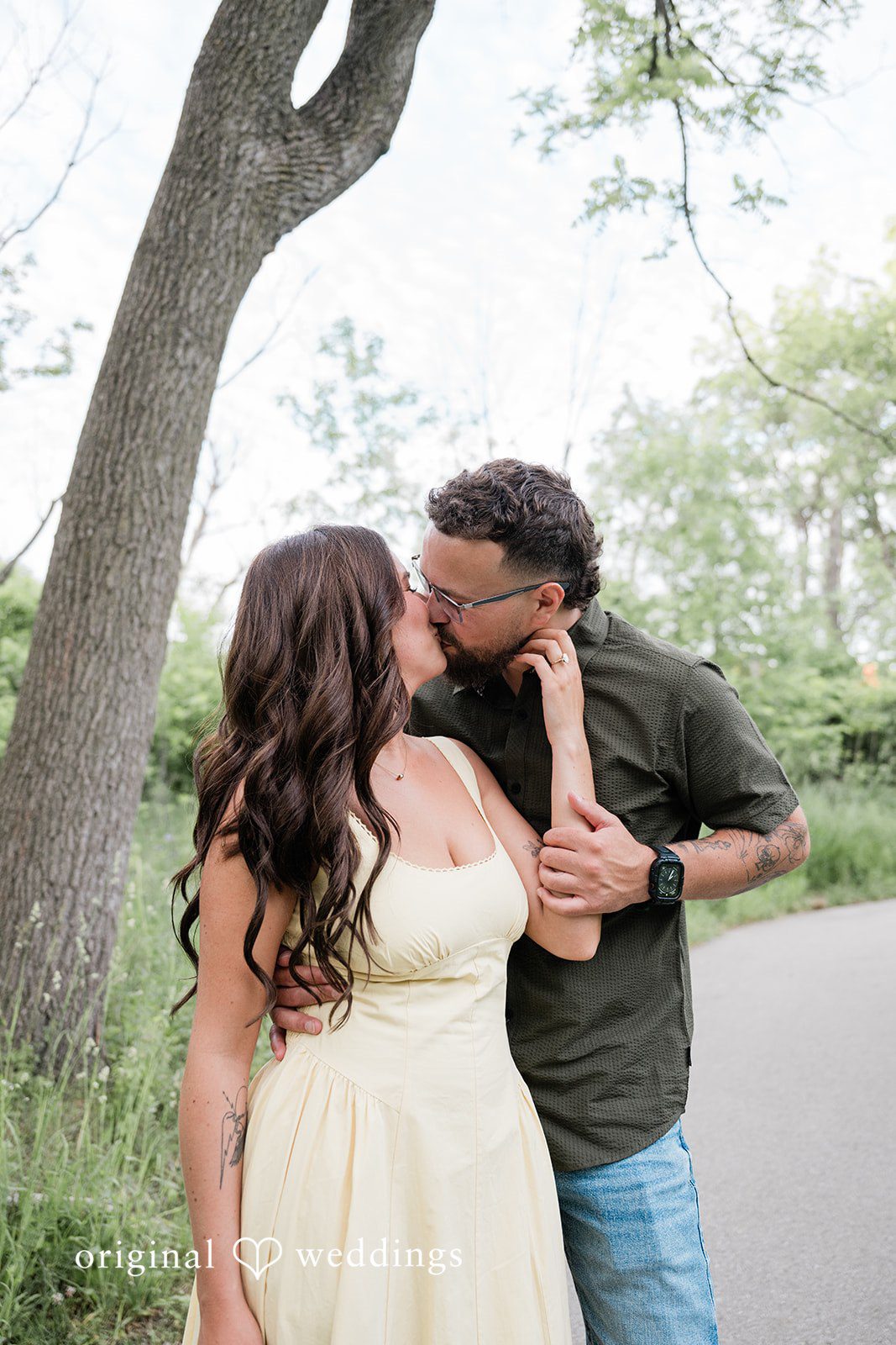 Andrea + Jordan A couple sharing a romantic kiss while leaning against a large tree trunk.