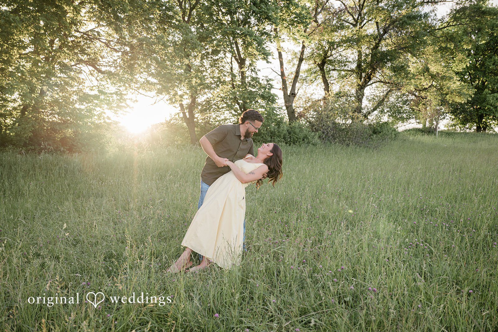 Andrea + Jordan A man dips a woman backwards during a romantic moment in a sunlit grassy field.