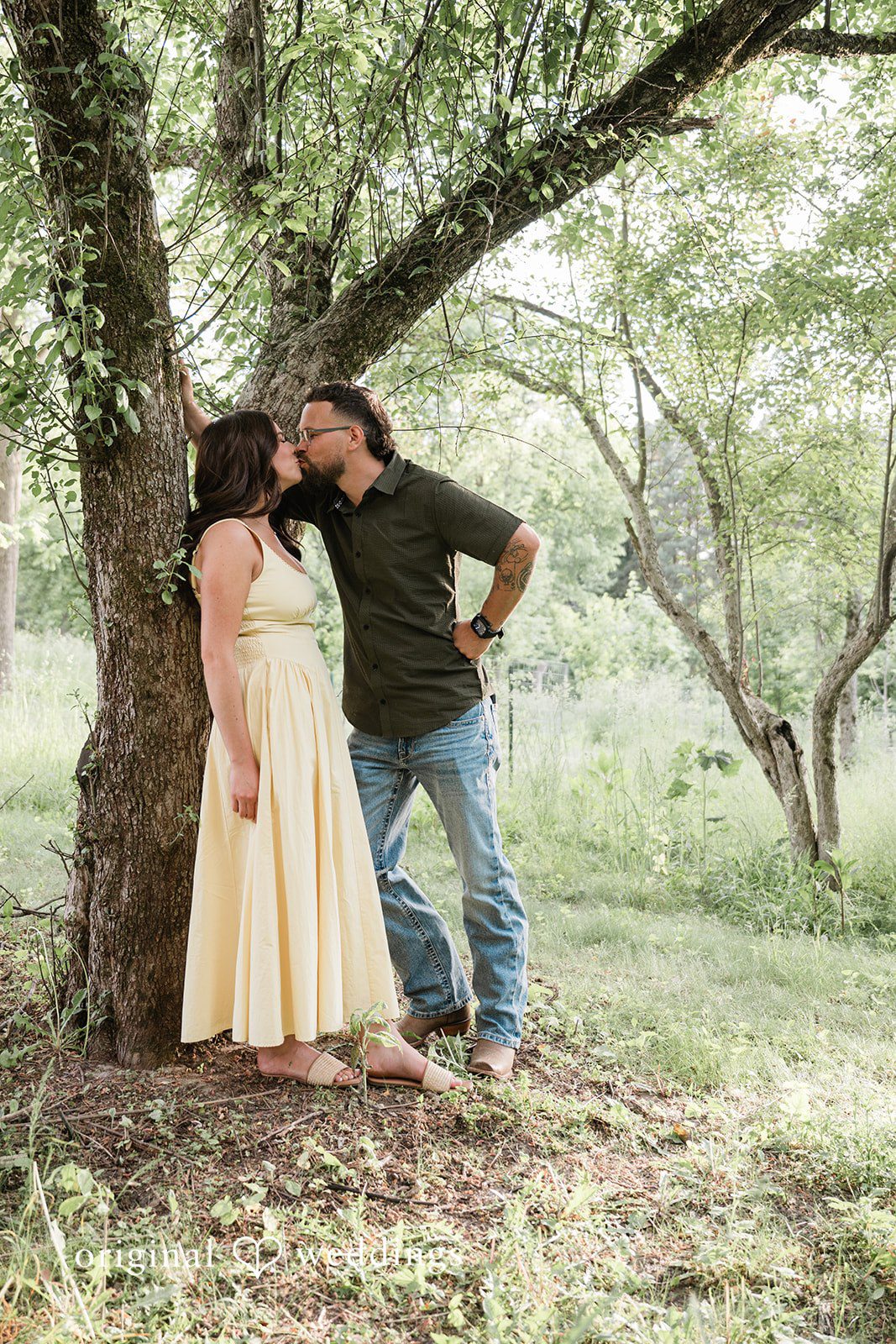 Andrea + Jordan A couple posing together while leaning against a large tree in a wooded area.