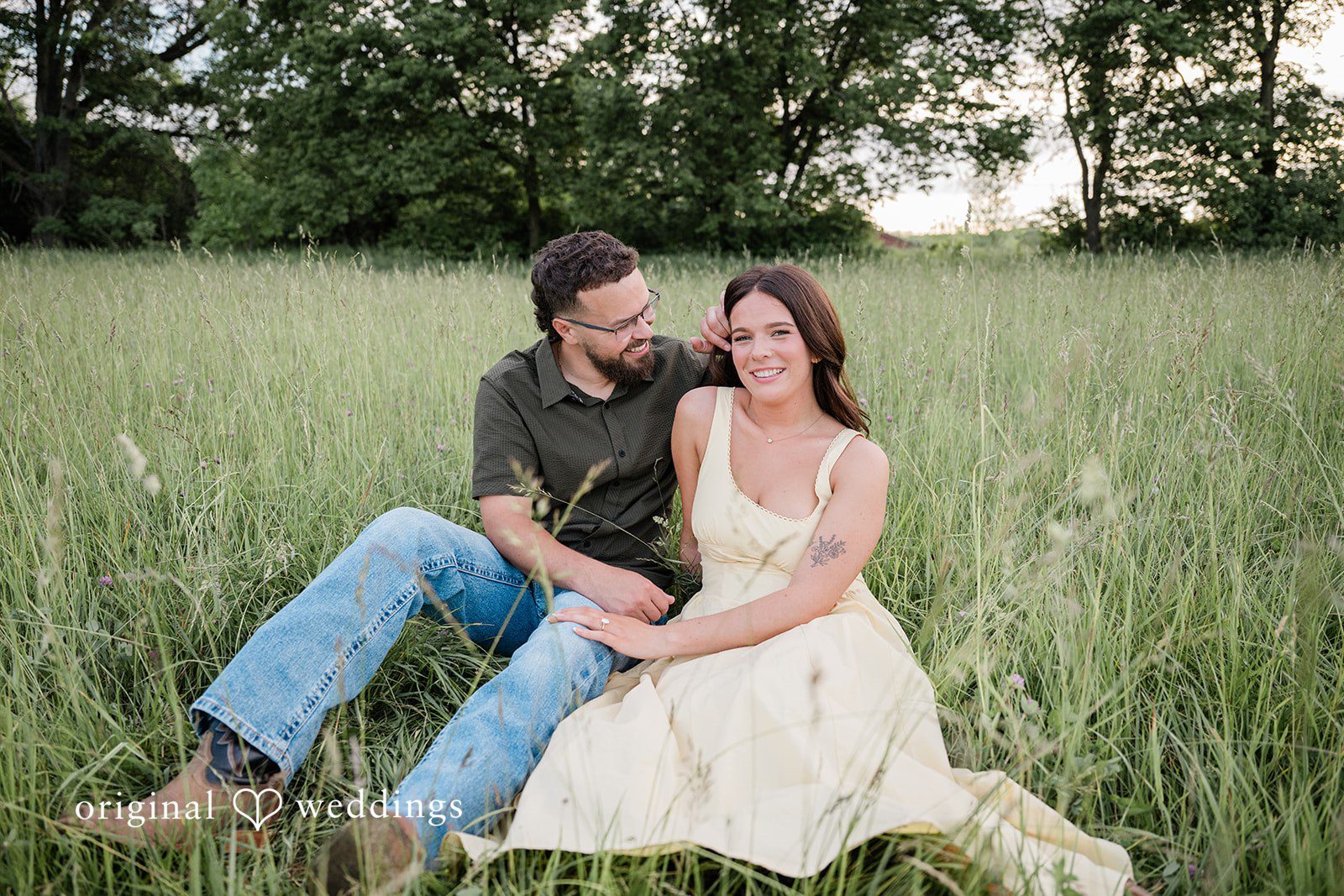 Andrea + Jordan A couple sitting together in a grassy field with the man leaning against a small hill.