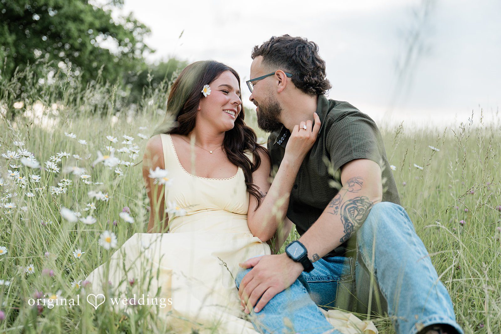 Andrea + Jordan A couple sitting closely together on a grassy hillside while sharing an intimate look.