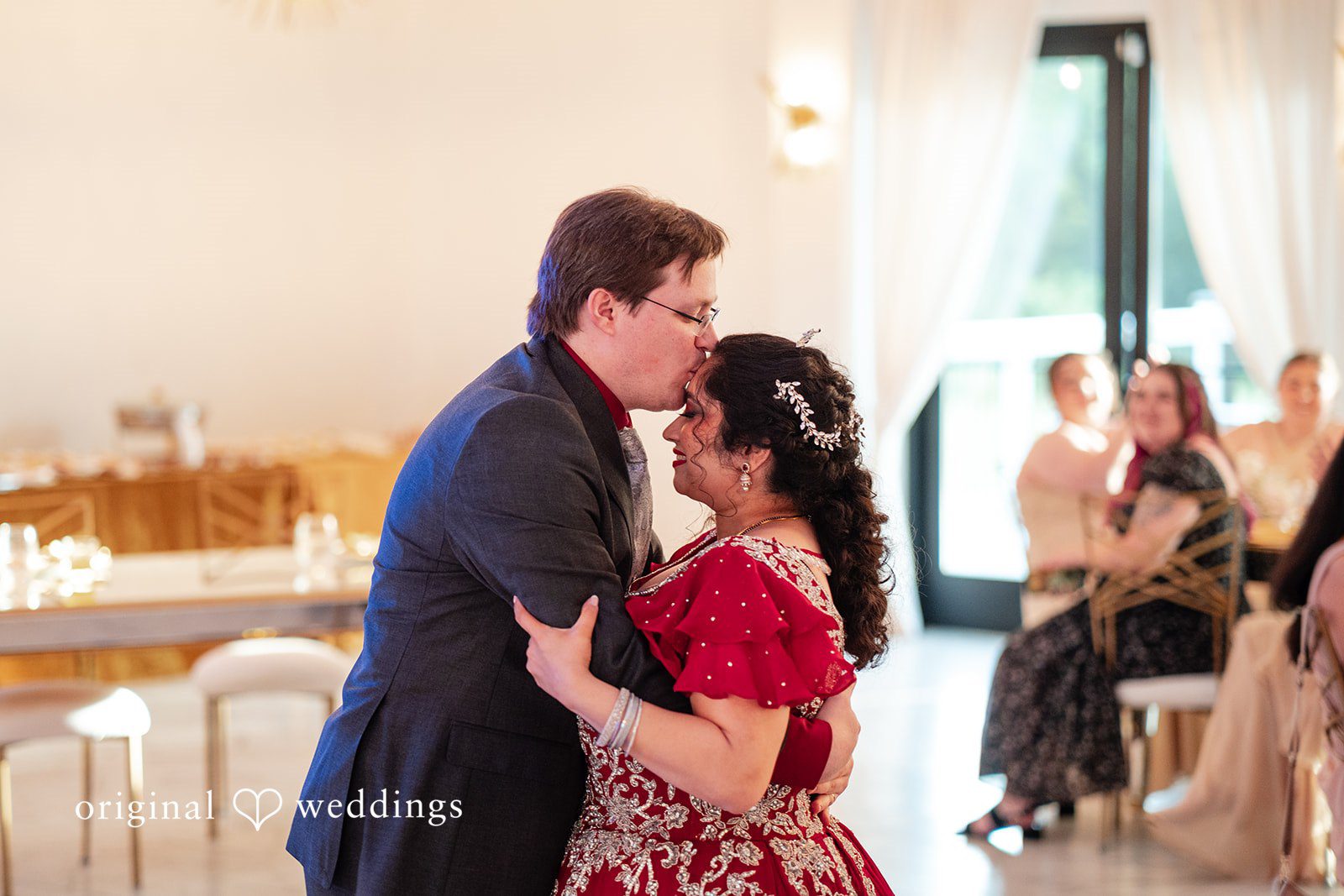 Anthony + Simi A groom gently kissing a bride's forehead at a reception.