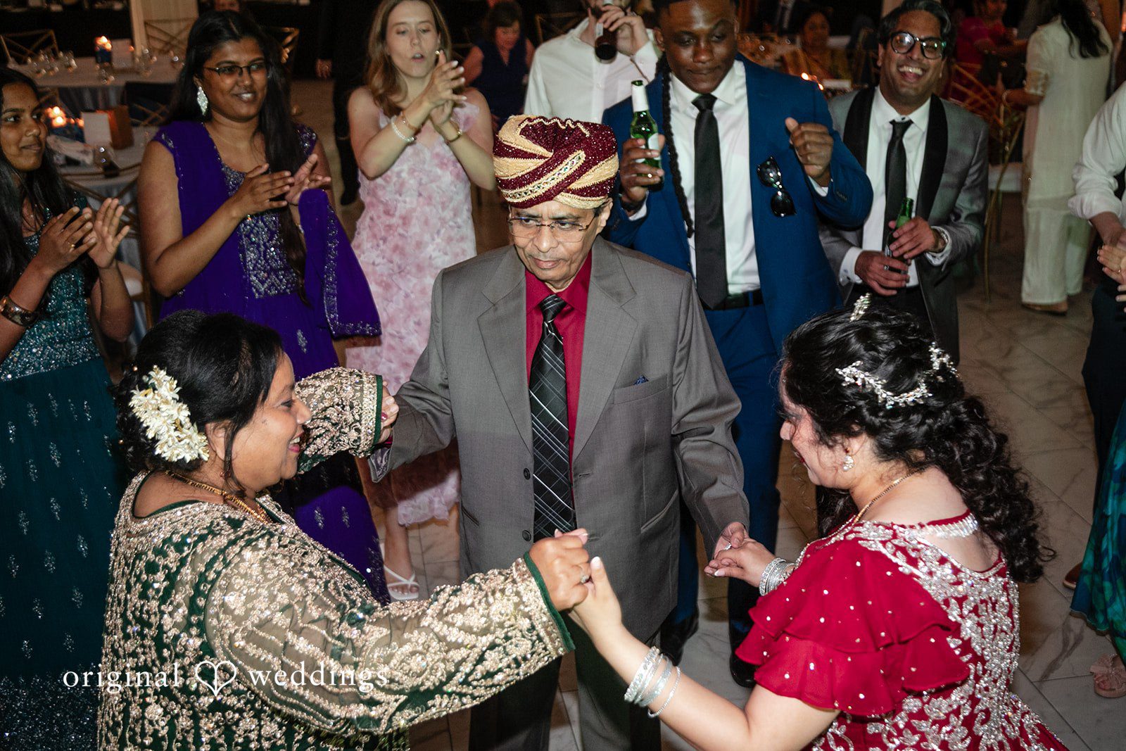 Anthony + Simi A group of people dancing and celebrating at a reception party.
