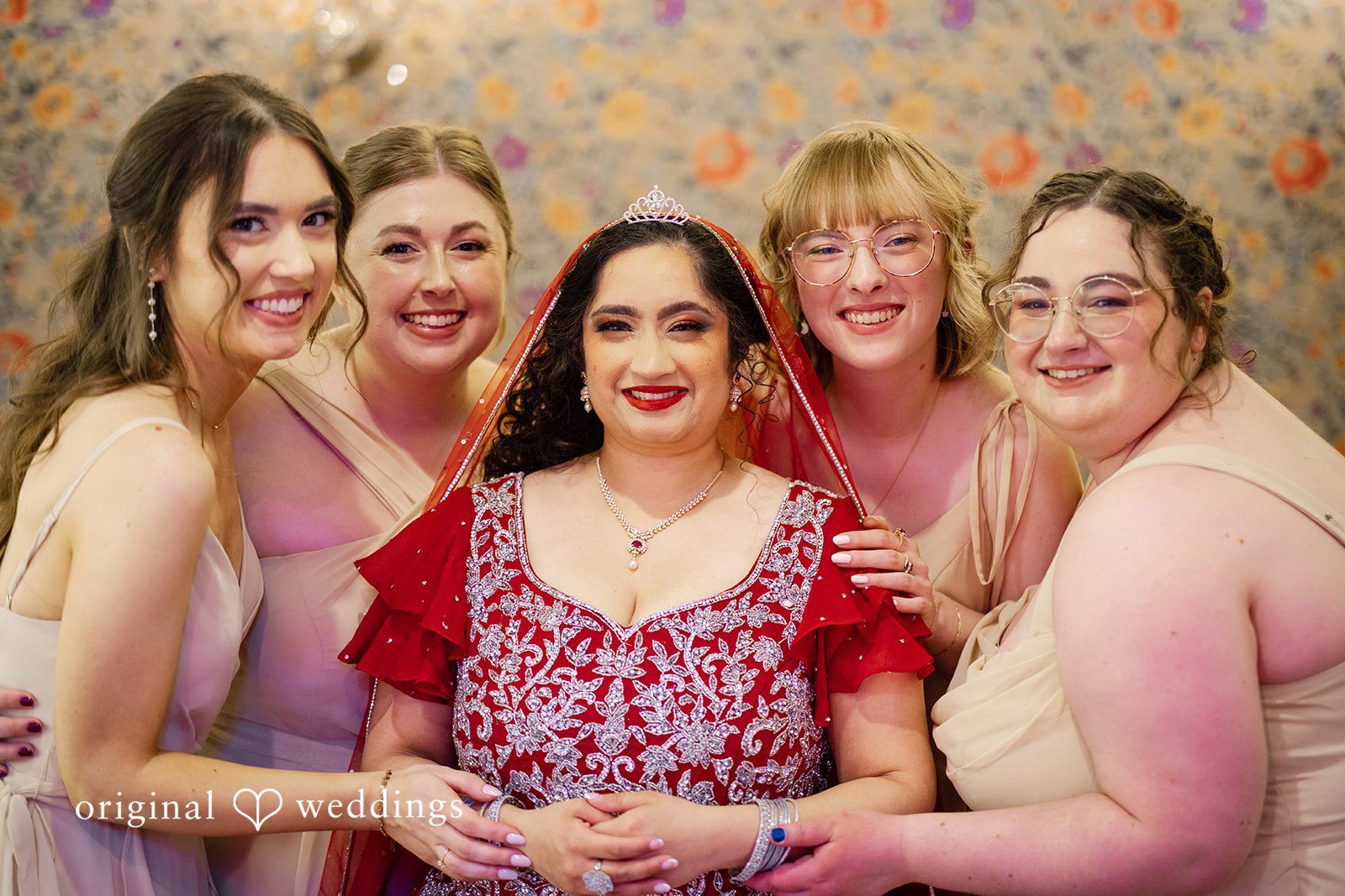 Anthony + Simi A bride in a red dress smiling while posing with Bridesmaid.