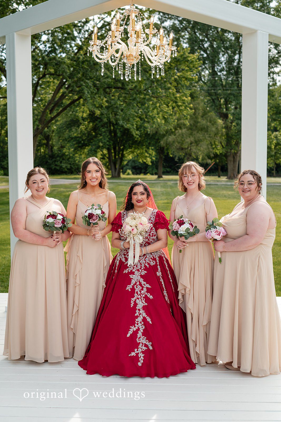 Anthony + Simi A bride in red standing with four bridesmaids in beige dresses at Revelry 675.