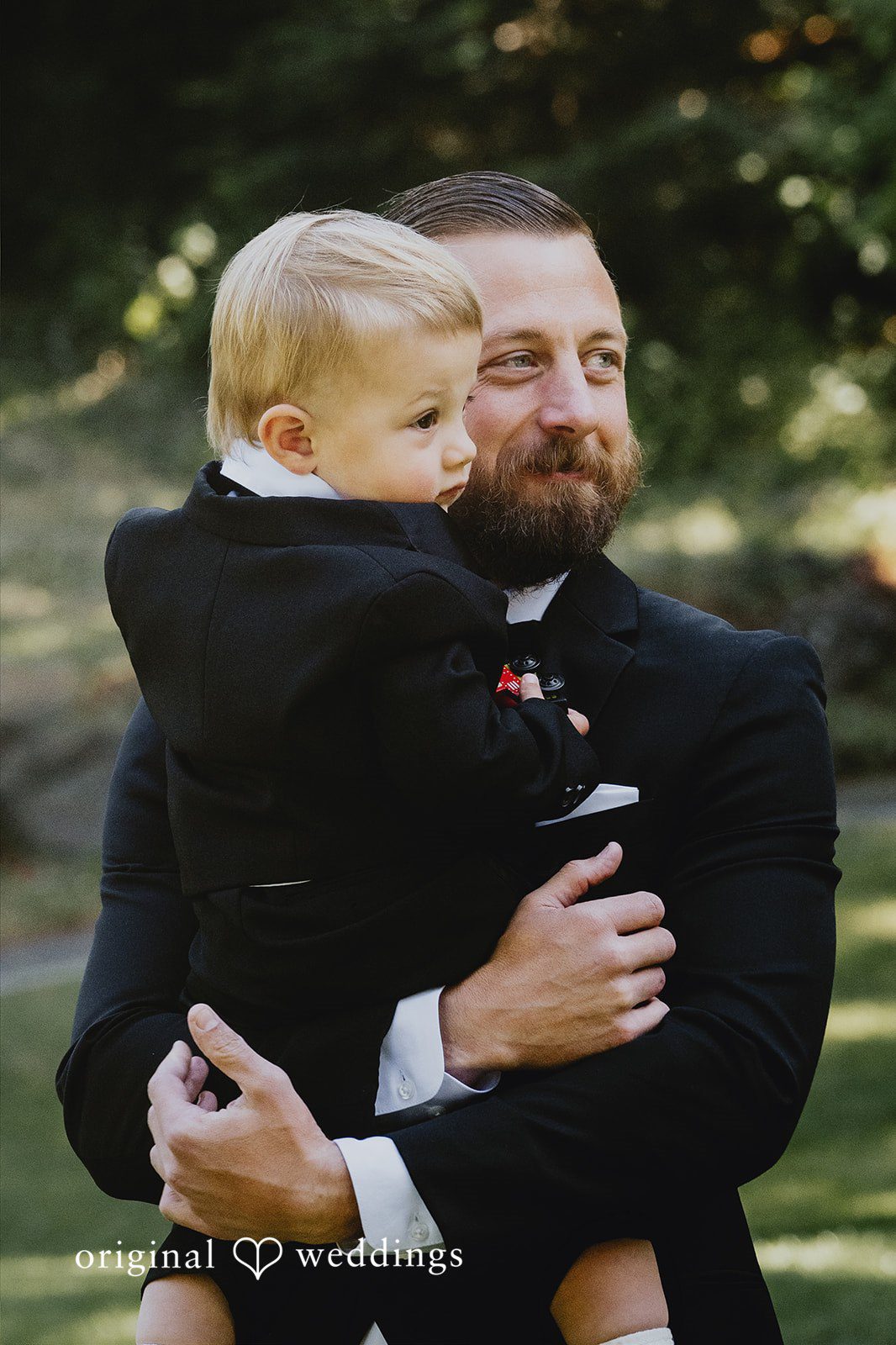 Kristina + Christopher Groom in a tuxedo holding a young boy in a matching outfit.