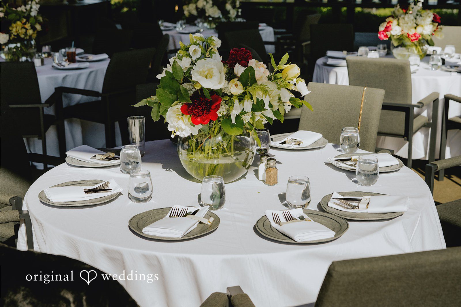 Kristina + Christopher Round reception table set with white linens, dinnerware, and a floral centerpiece.