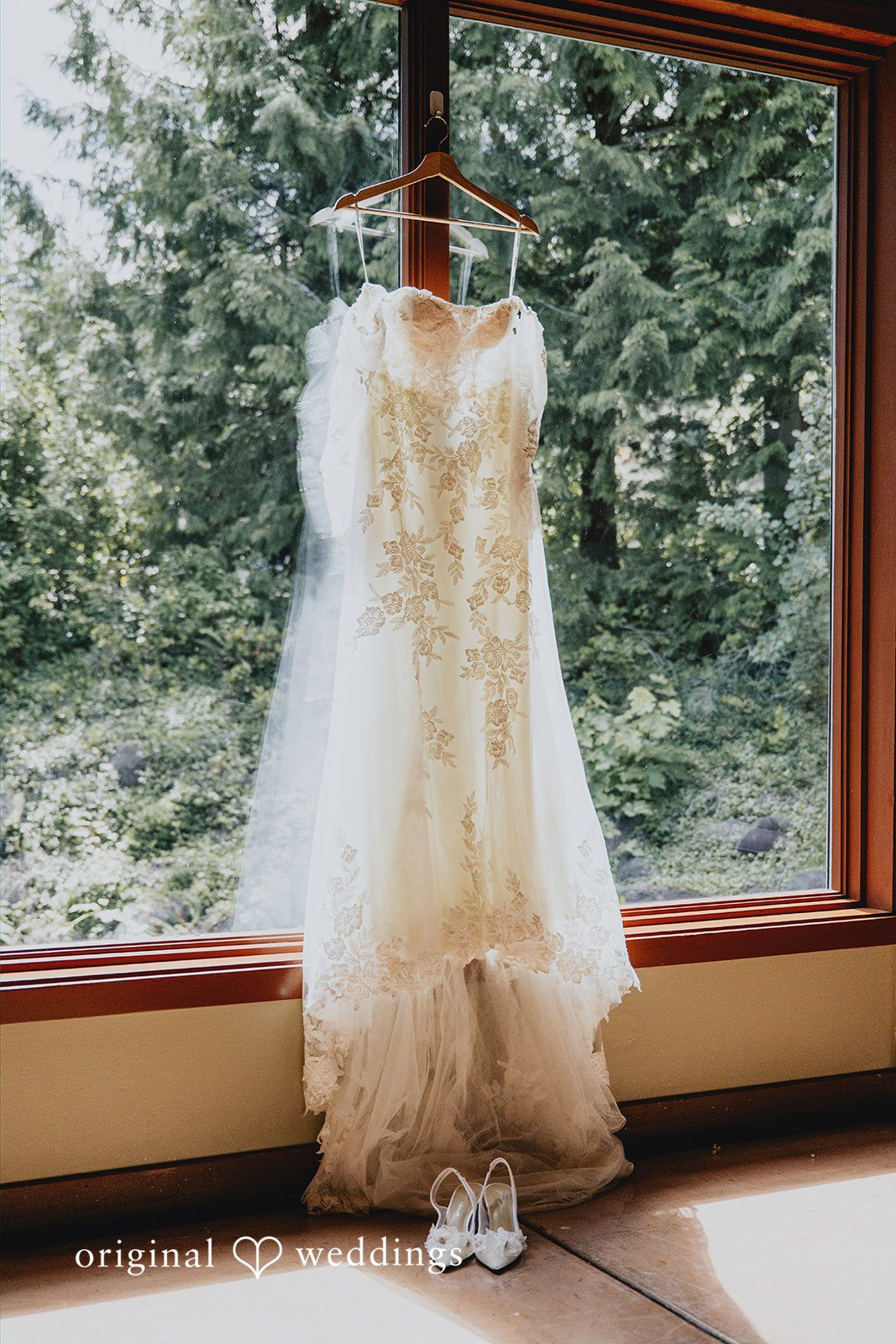 Kristina + Christopher White wedding dress hanging in front of a large window.