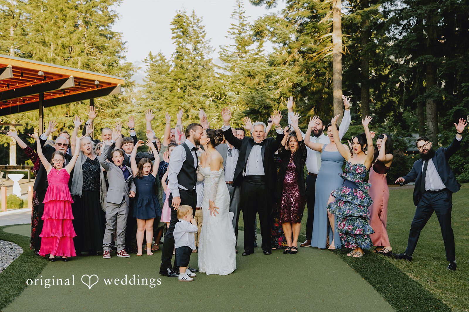 Kristina + Christopher A large group of wedding guests cheering with their hands raised.
