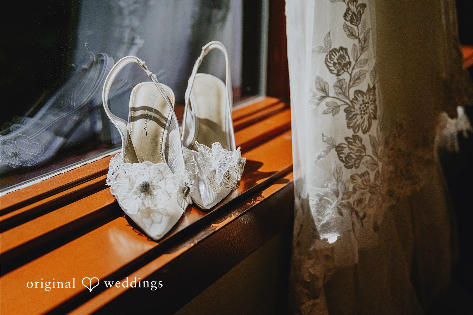 Kristina + Christopher White bridal heels on a window sill next to lace fabric.