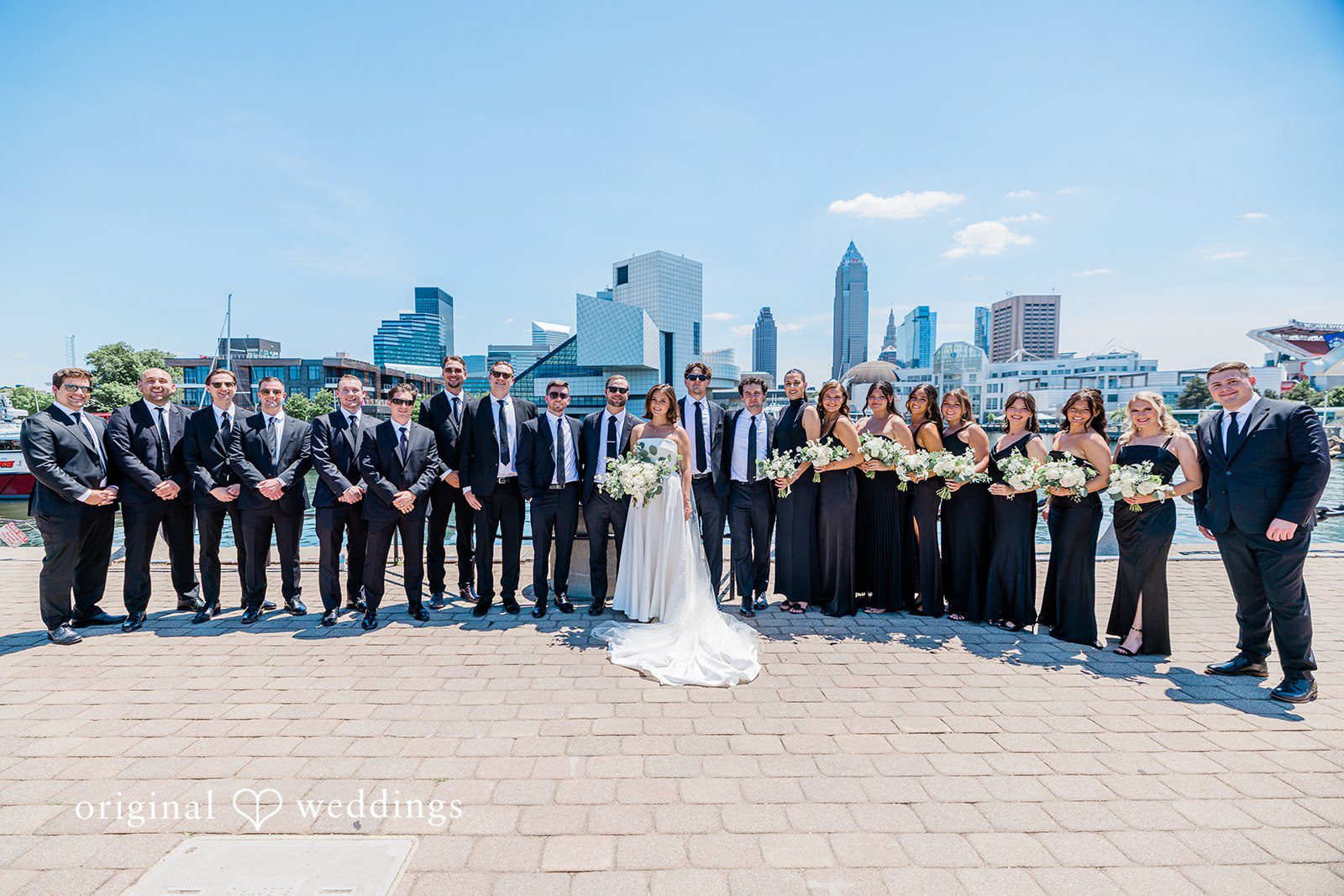 Luke + Madison Bride, groom, bridesmaids and groomsmen posing with the city skyline at St. Clair Ballroom captured by Cleveland Wedding Photographers from Original Weddings.