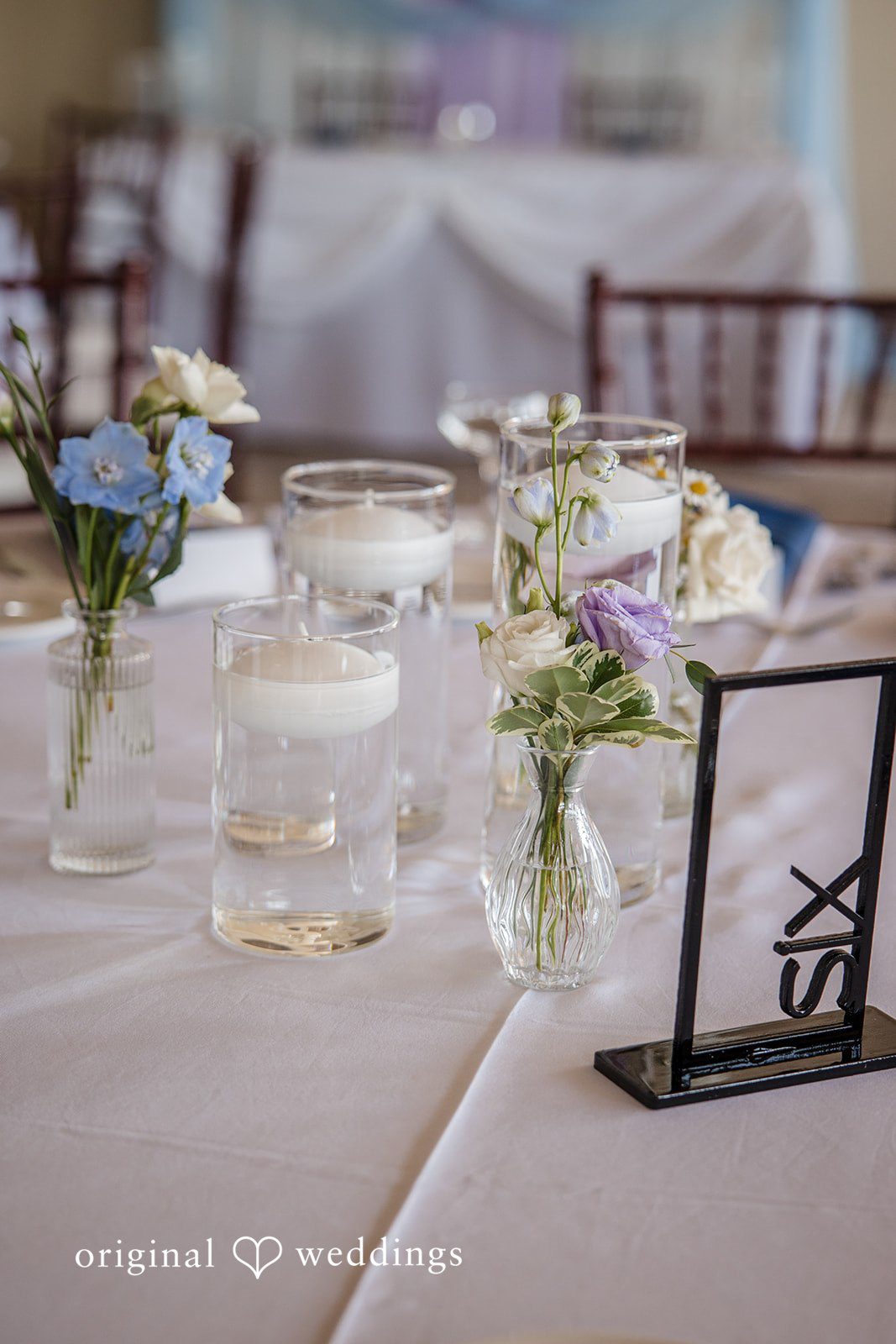 James + Nora Close-up of a table centerpiece with a glass vase, floral arrangement, and candles at St. Clair Inn
