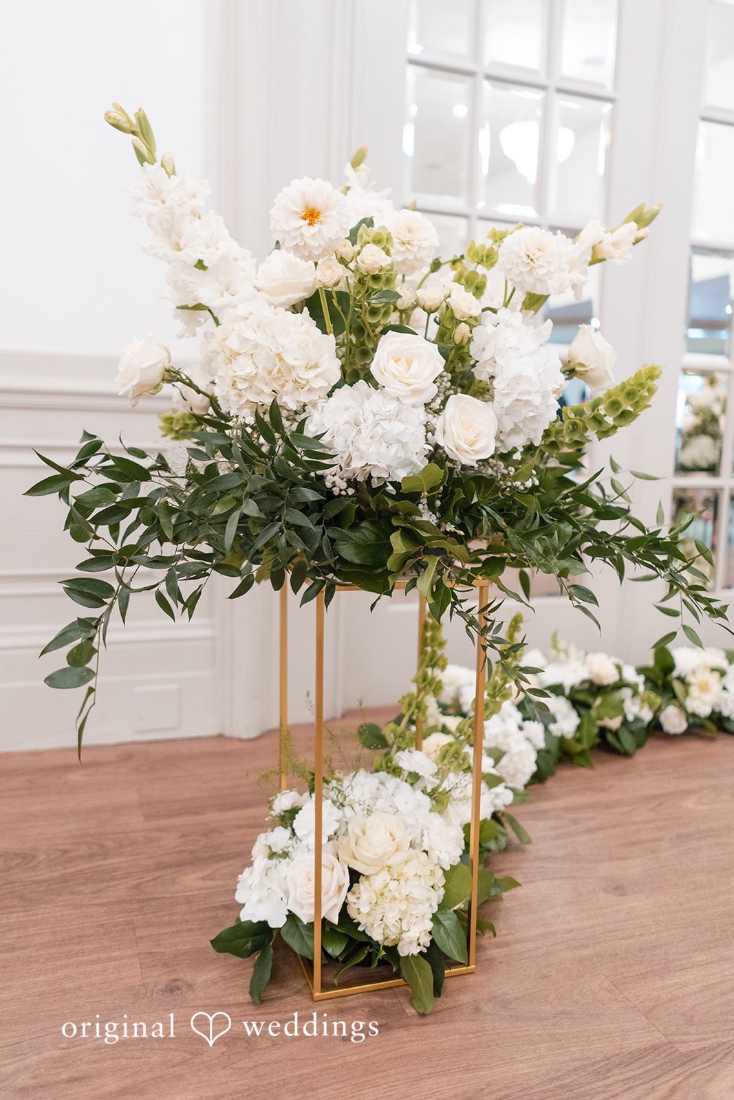 Elegant white floral arrangement displayed on a gold stand for the wedding ceremony
