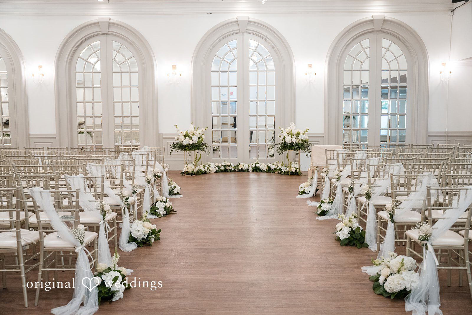 Elegant indoor wedding ceremony setup at Sterling Hotel with white floral décor and aisle arrangements.