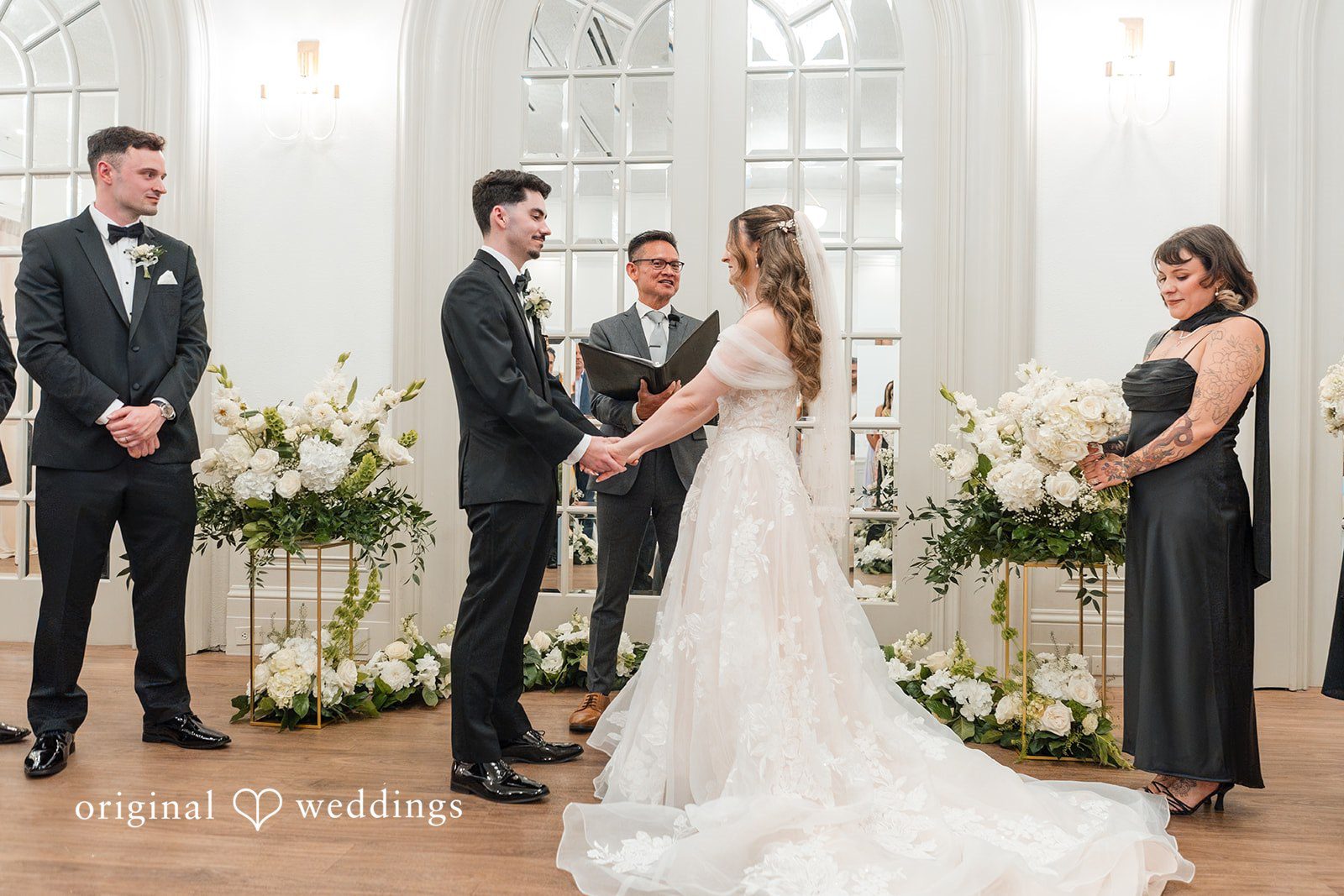 Bride and groom holding hands during their wedding ceremony surrounded by elegant white florals