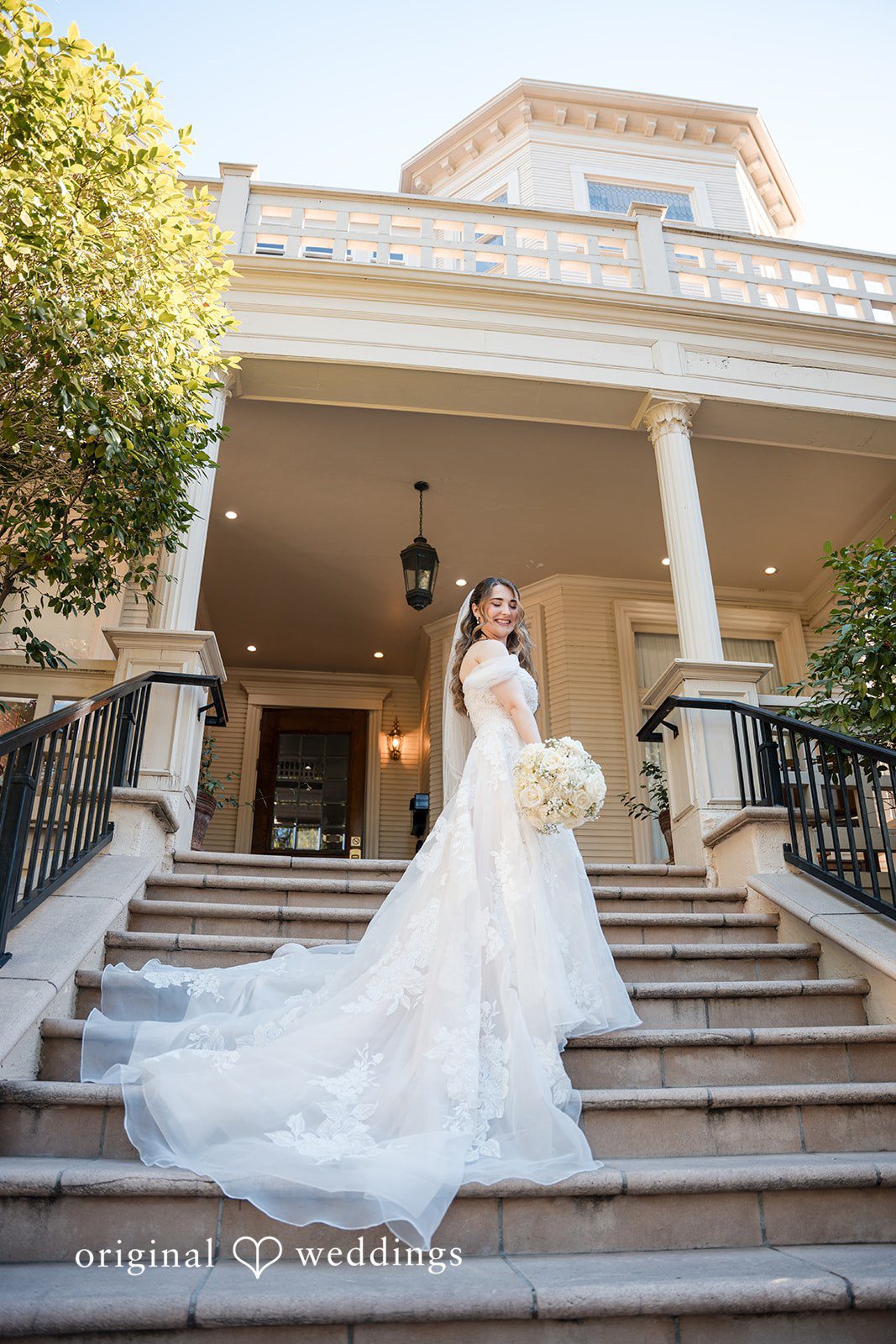 Bride standing gracefully on the grand staircase holding a white rose bouquet