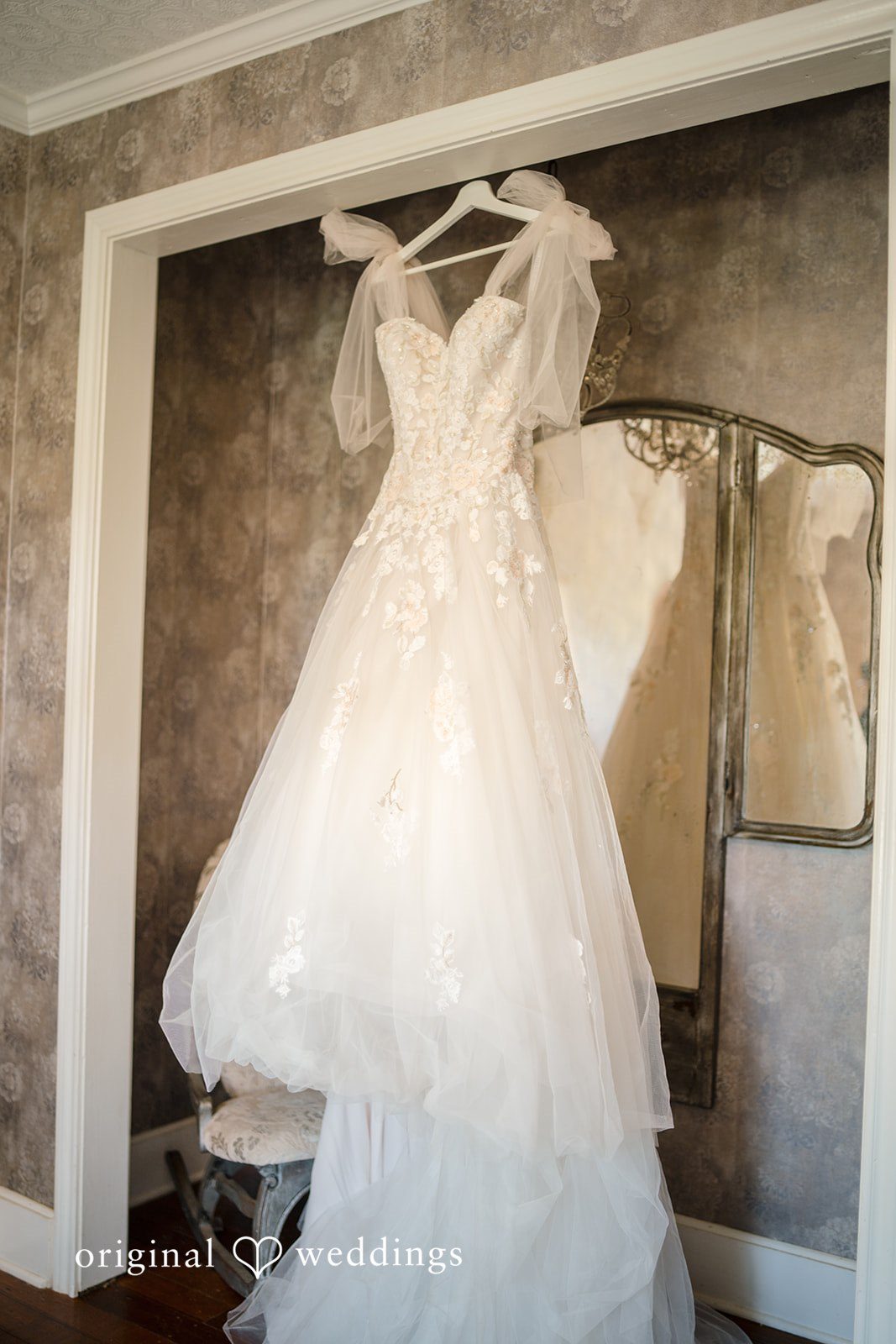 Morgan + Luke A white tulle wedding dress hangs on display near a window.