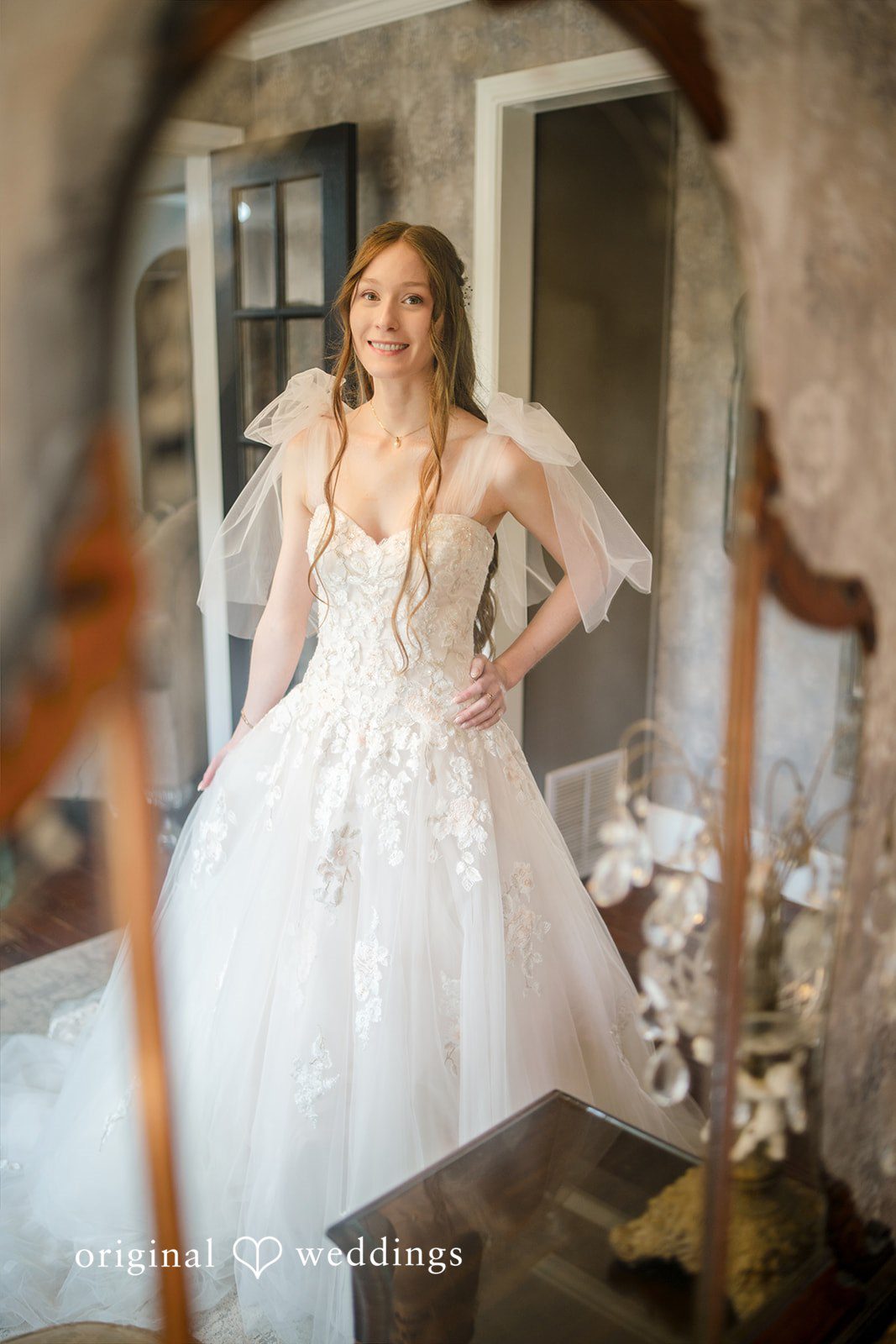 Morgan + Luke A bride poses elegantly in her full white gown near a mirror.