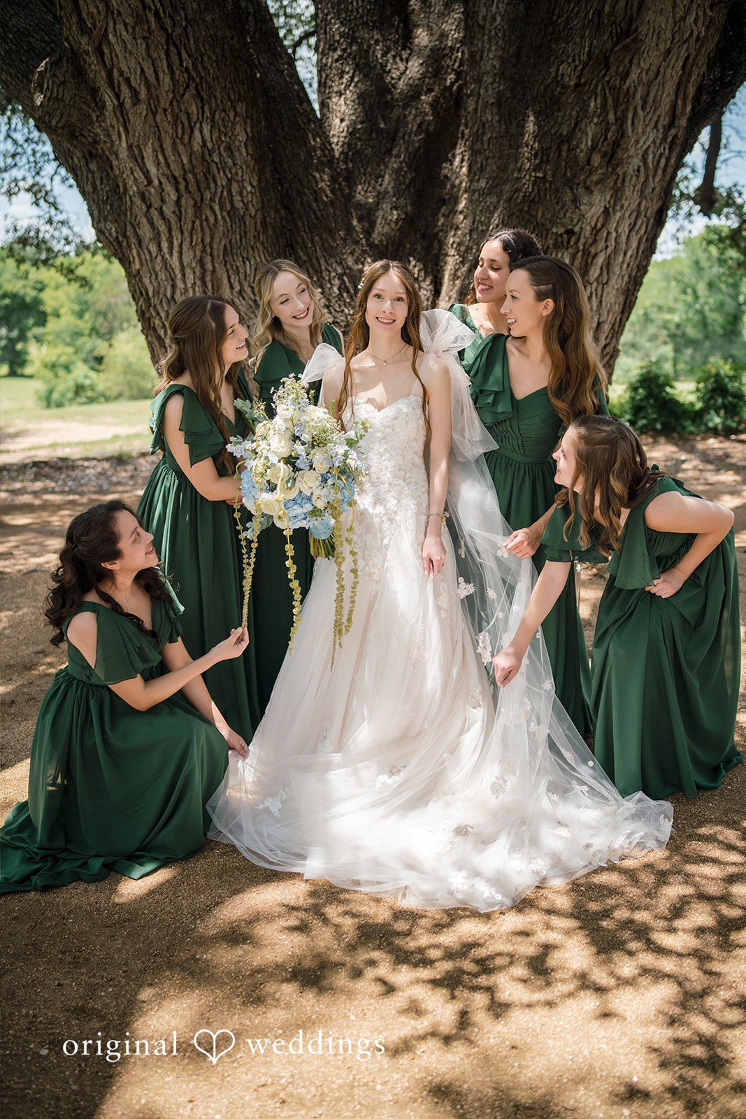 Morgan + Luke Bridesmaids in dark green dresses adjust the long train of a bride's gown.
