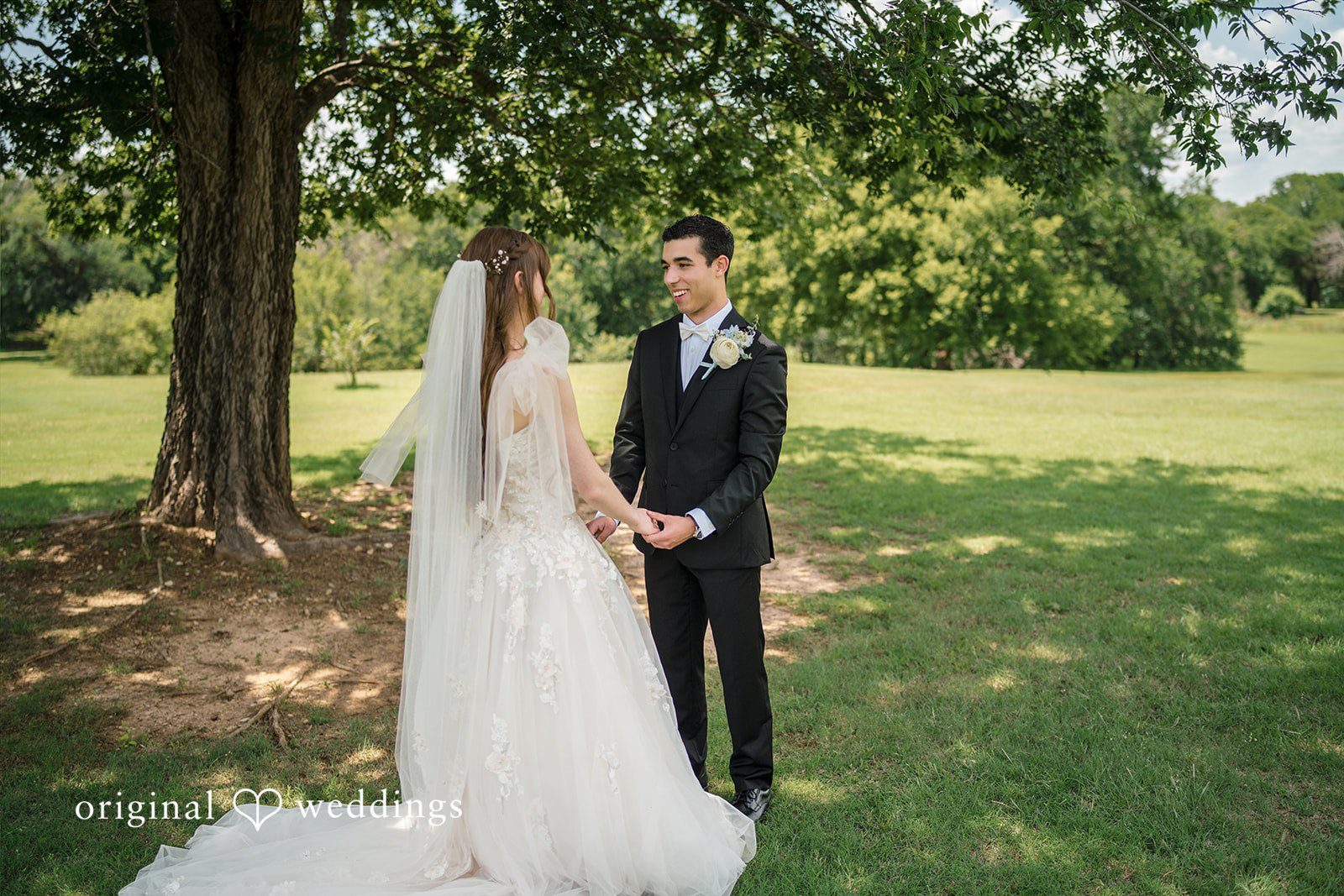 Morgan + Luke A bride and groom hold hands while standing face-to-face on a lawn.