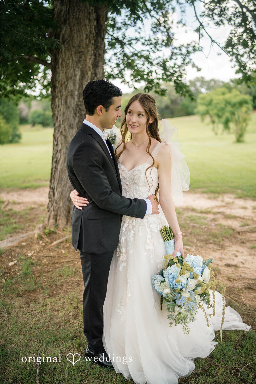 Morgan + Luke A groom embraces a bride holding a blue and white flower bouquet.